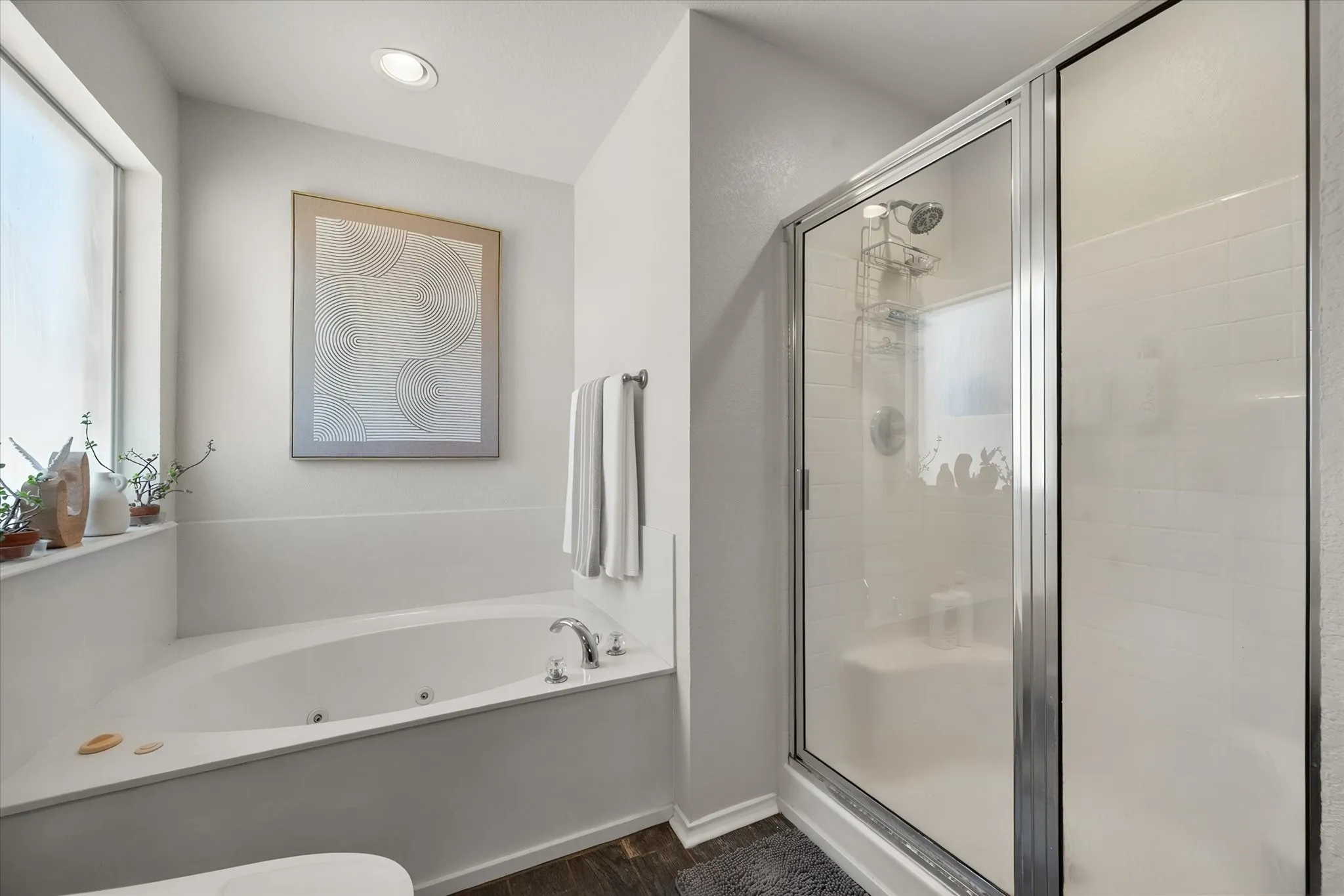 Built-in jetted tub with chrome fixtures, enclosed shower with glass door and white subway tile, wood-finish flooring, and recessed ceiling lighting