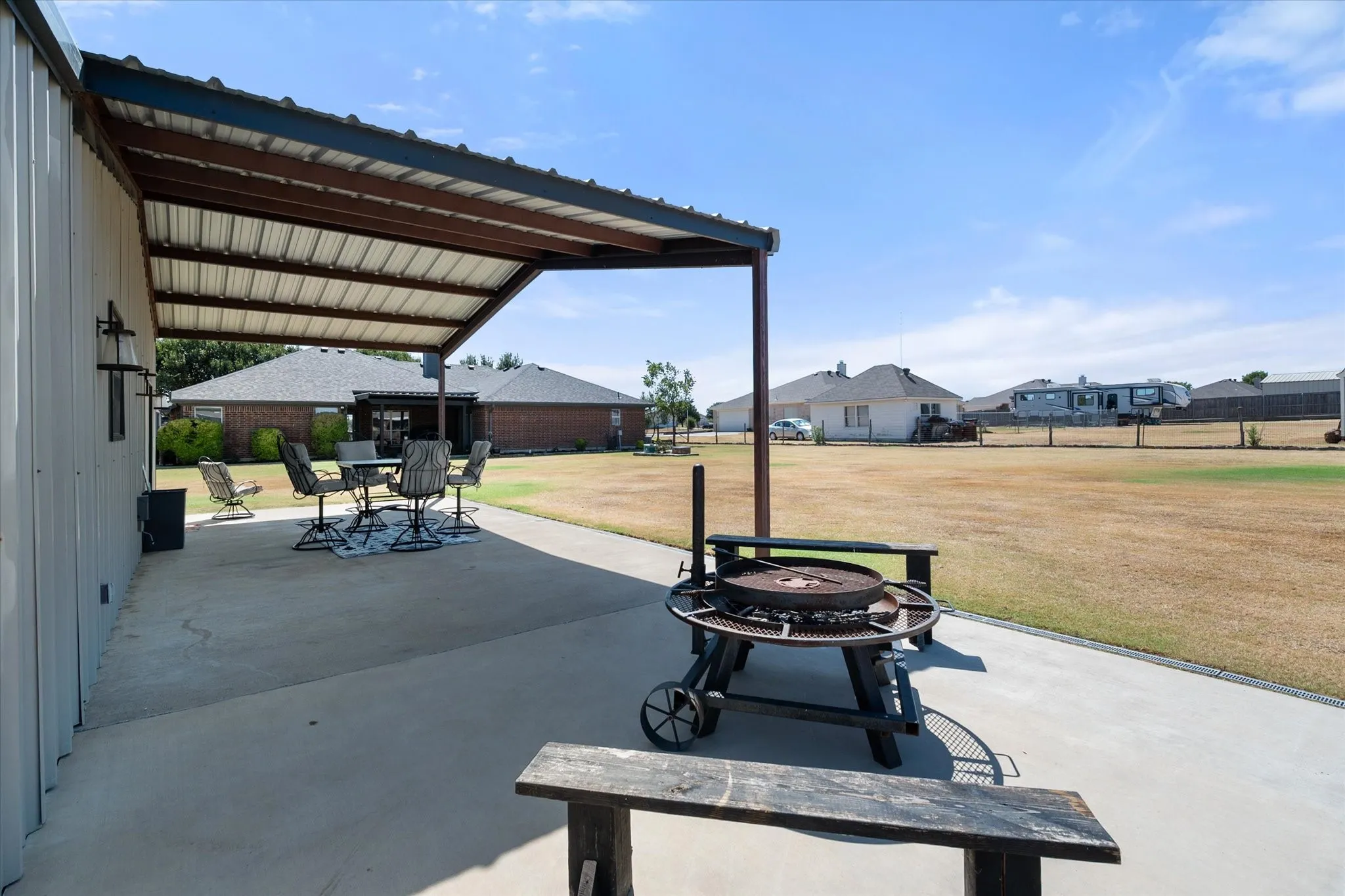 Expansive concrete patio with a metal awning covering a portion of the space   Overlooking the back yard