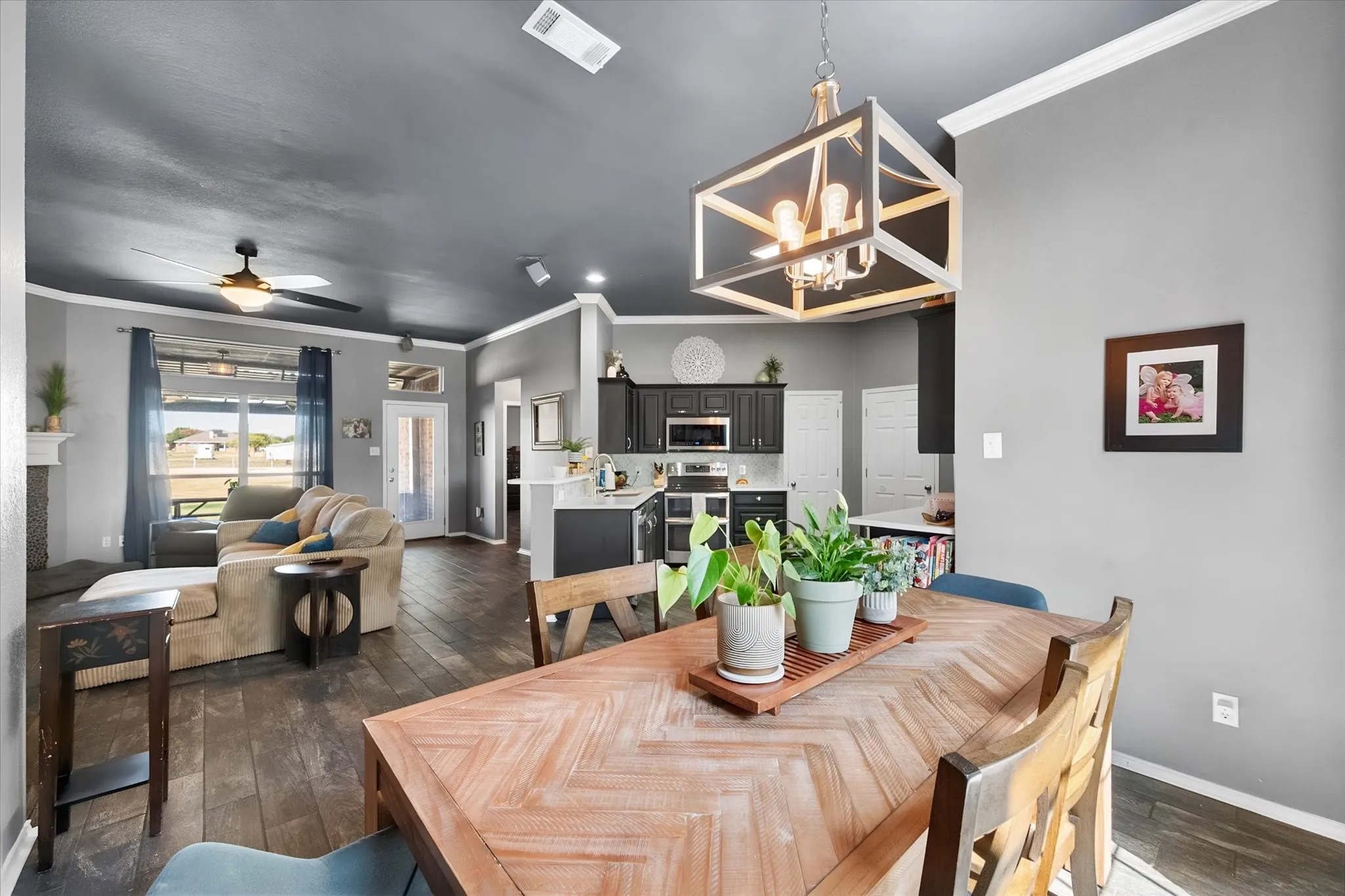 Open-concept living space with dark wood-finish flooring, white crown molding, a ceiling fan, and a contemporary chandelier