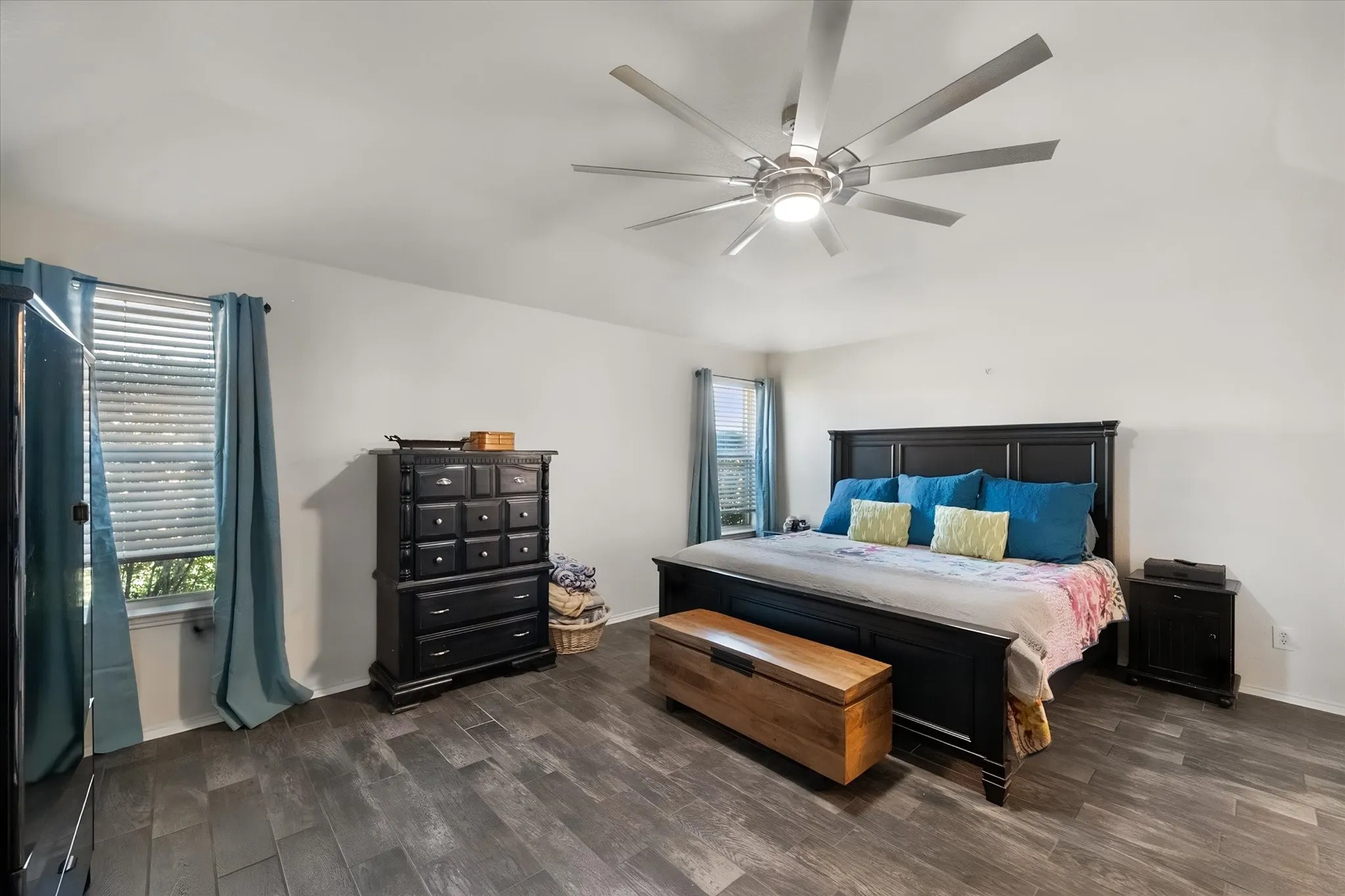 Spacious room featuring wood-finish flooring, white walls, and an included ceiling fan