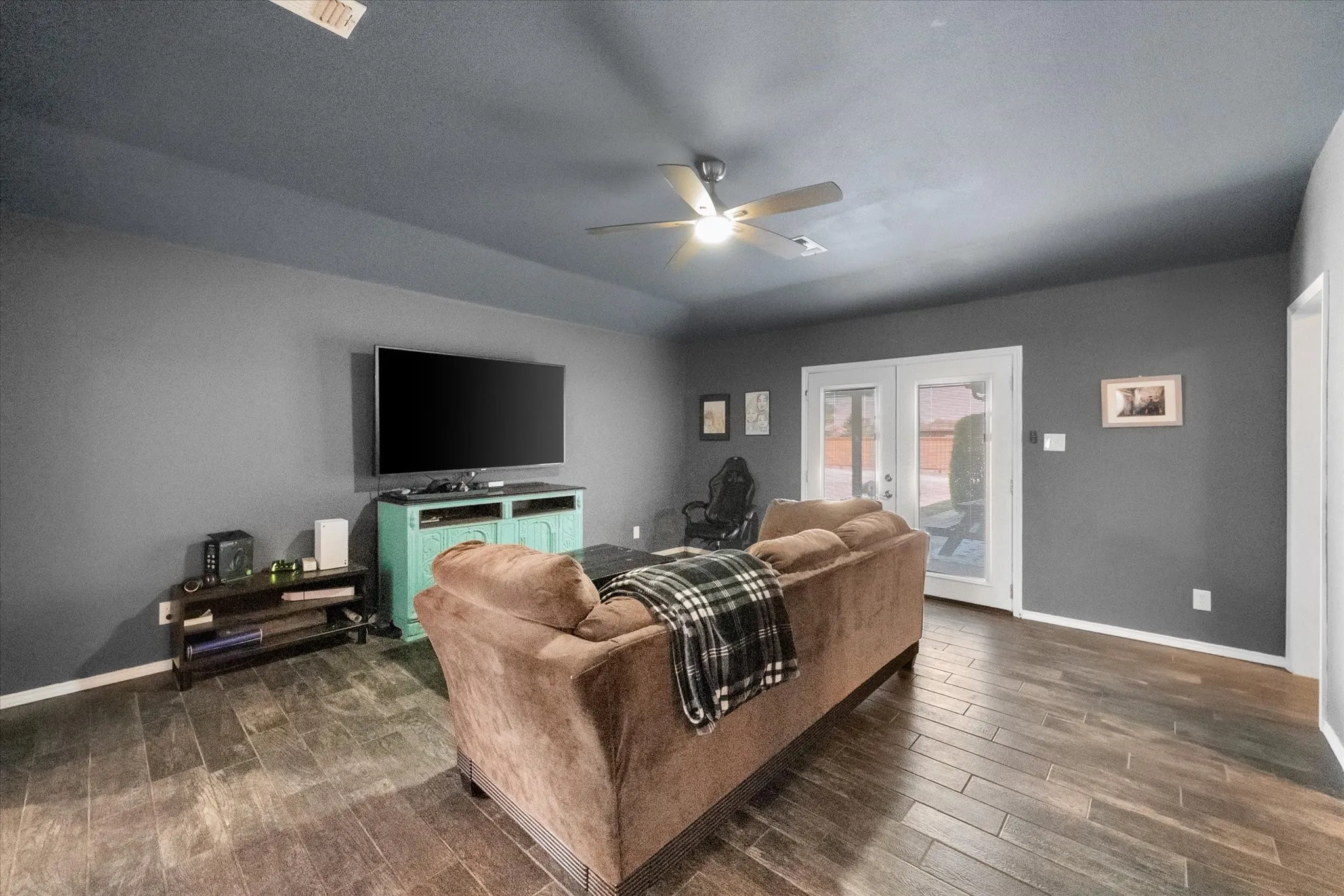 Wood-finish flooring throughout, ceiling fan with integrated lighting, and white French doors with upper glass panels