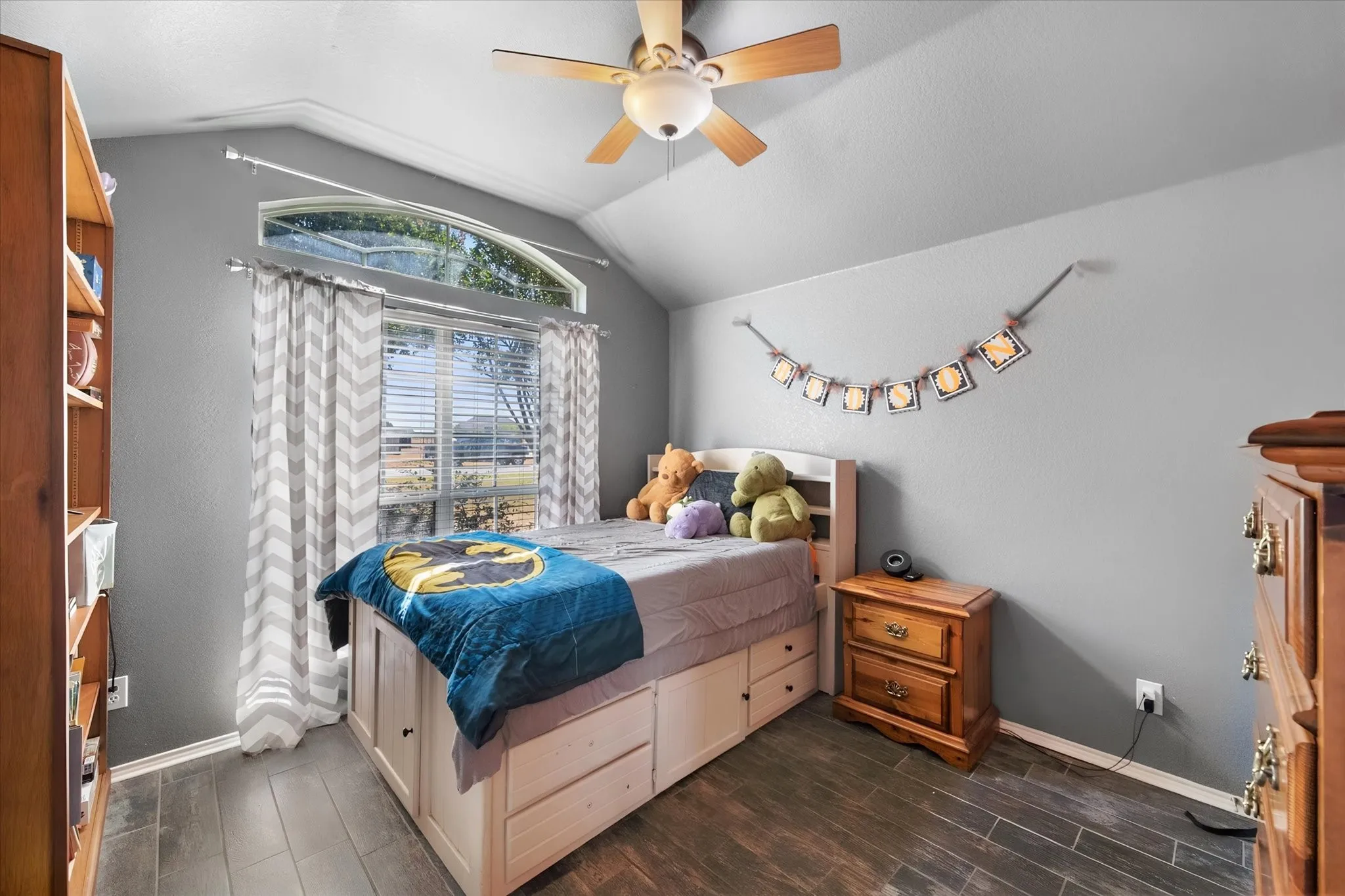 Vaulted ceiling with crown molding, wood-finish flooring, ceiling fan with light, and arched transom window