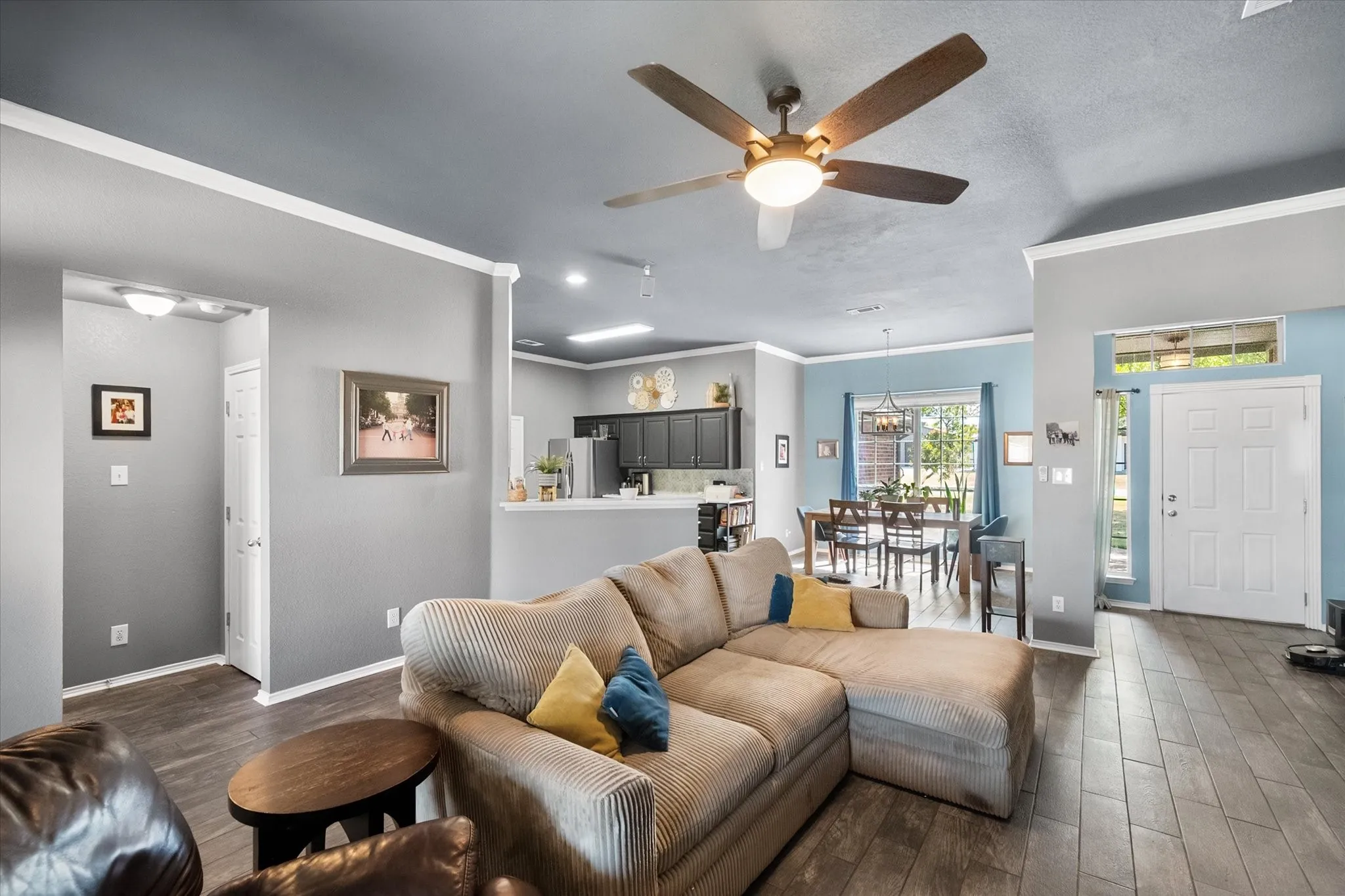 Open-concept living area with wood-finish flooring, a ceiling fan with integrated lighting, and crown molding