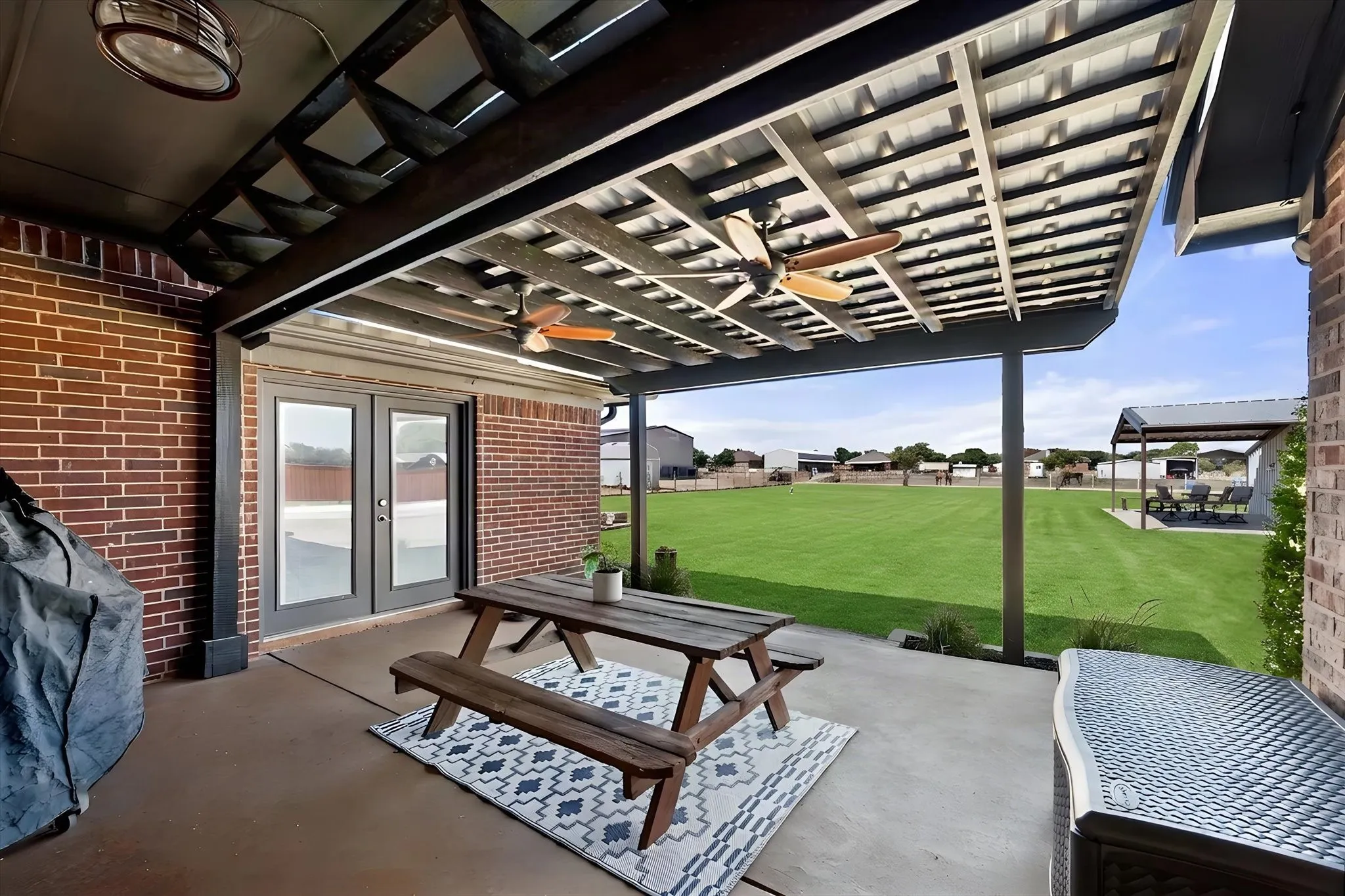 Covered patio with dual ceiling fans, brick exterior, concrete patio, and French doors