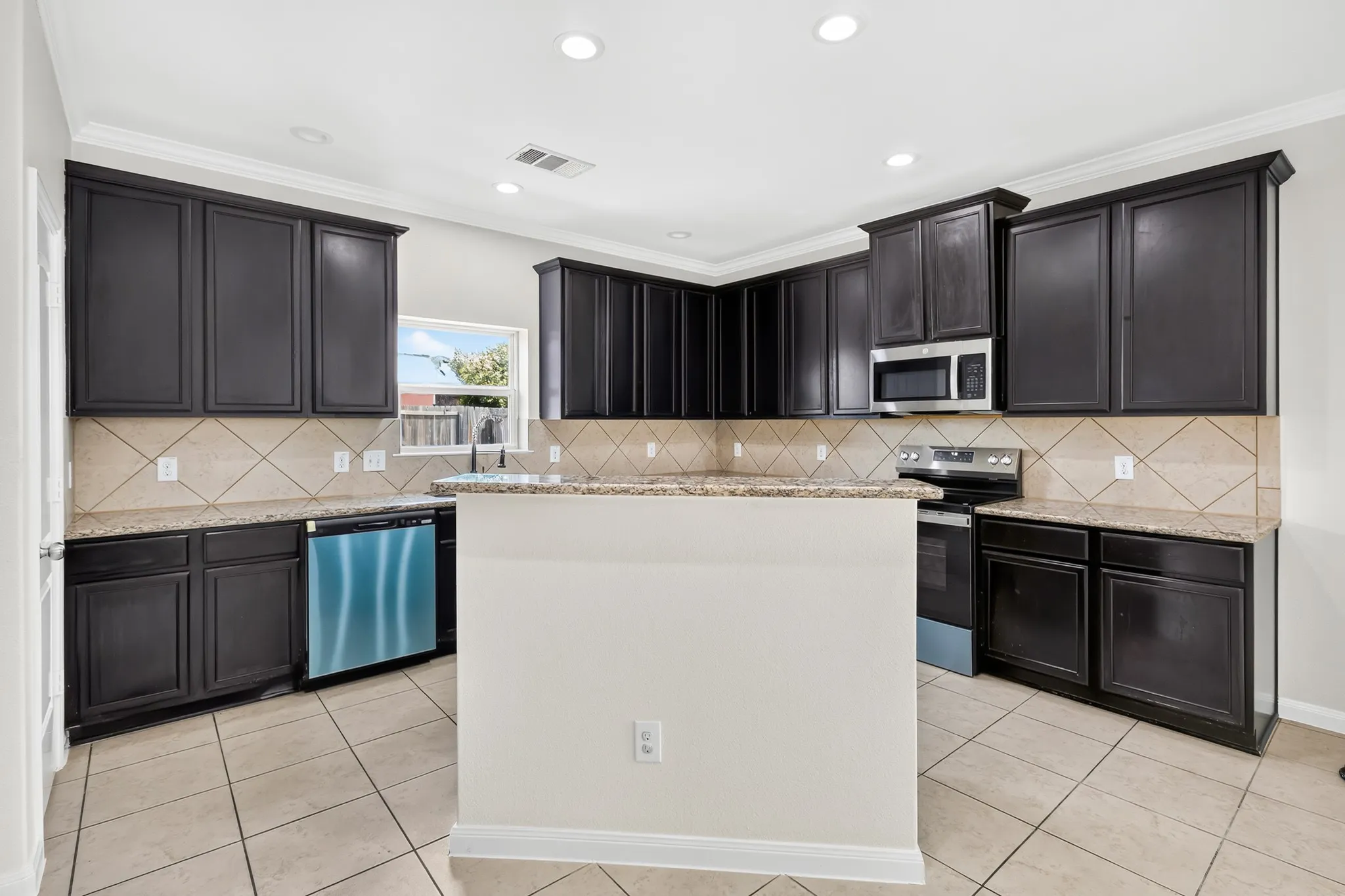 Dark wood-finish cabinetry, light-toned granite countertops, tile backsplash, stainless steel appliances, and recessed lighting