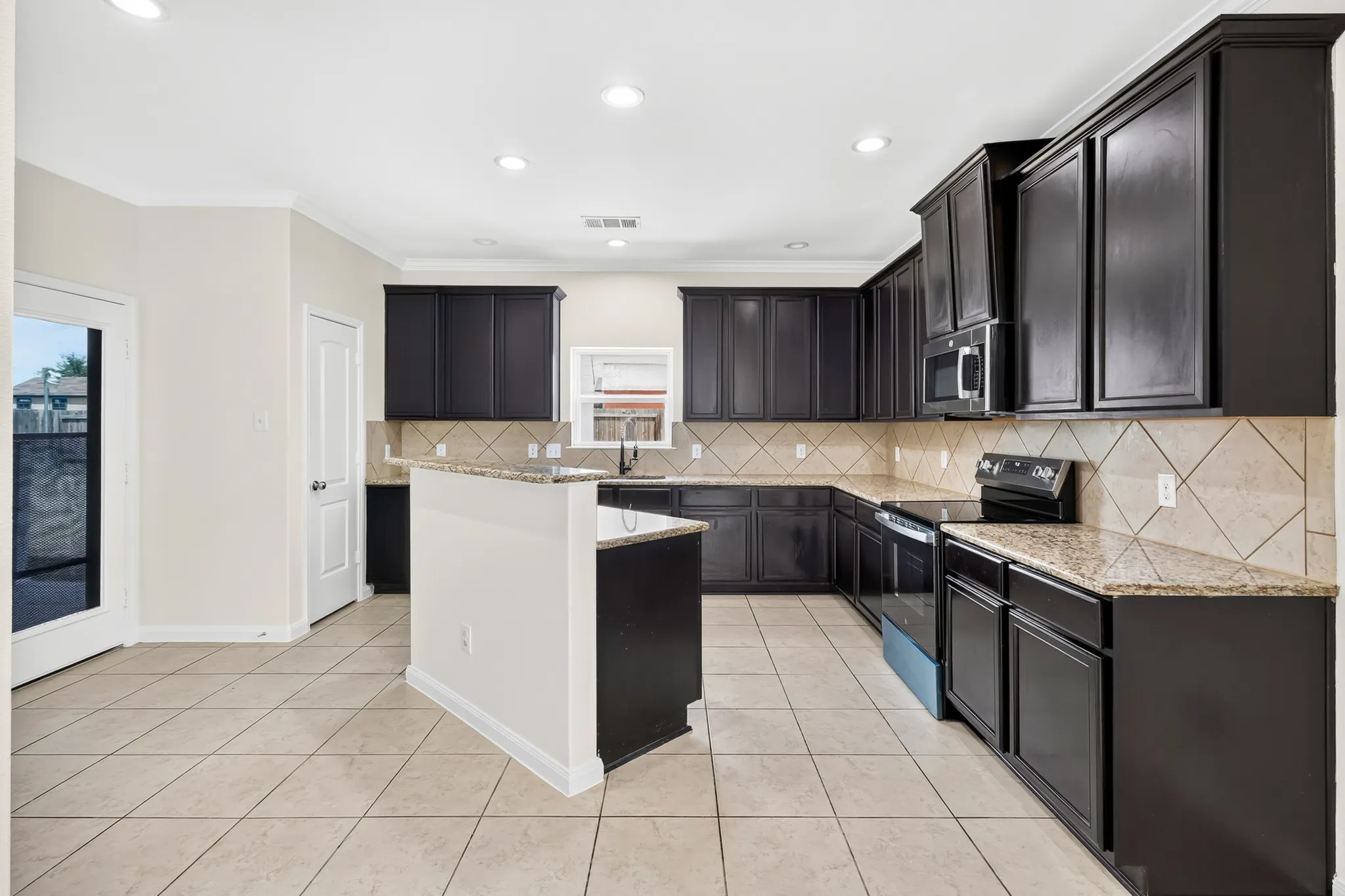 Kitchen featuring dark wood-finish cabinetry, light-toned tile flooring, granite countertops, and a tile backsplash