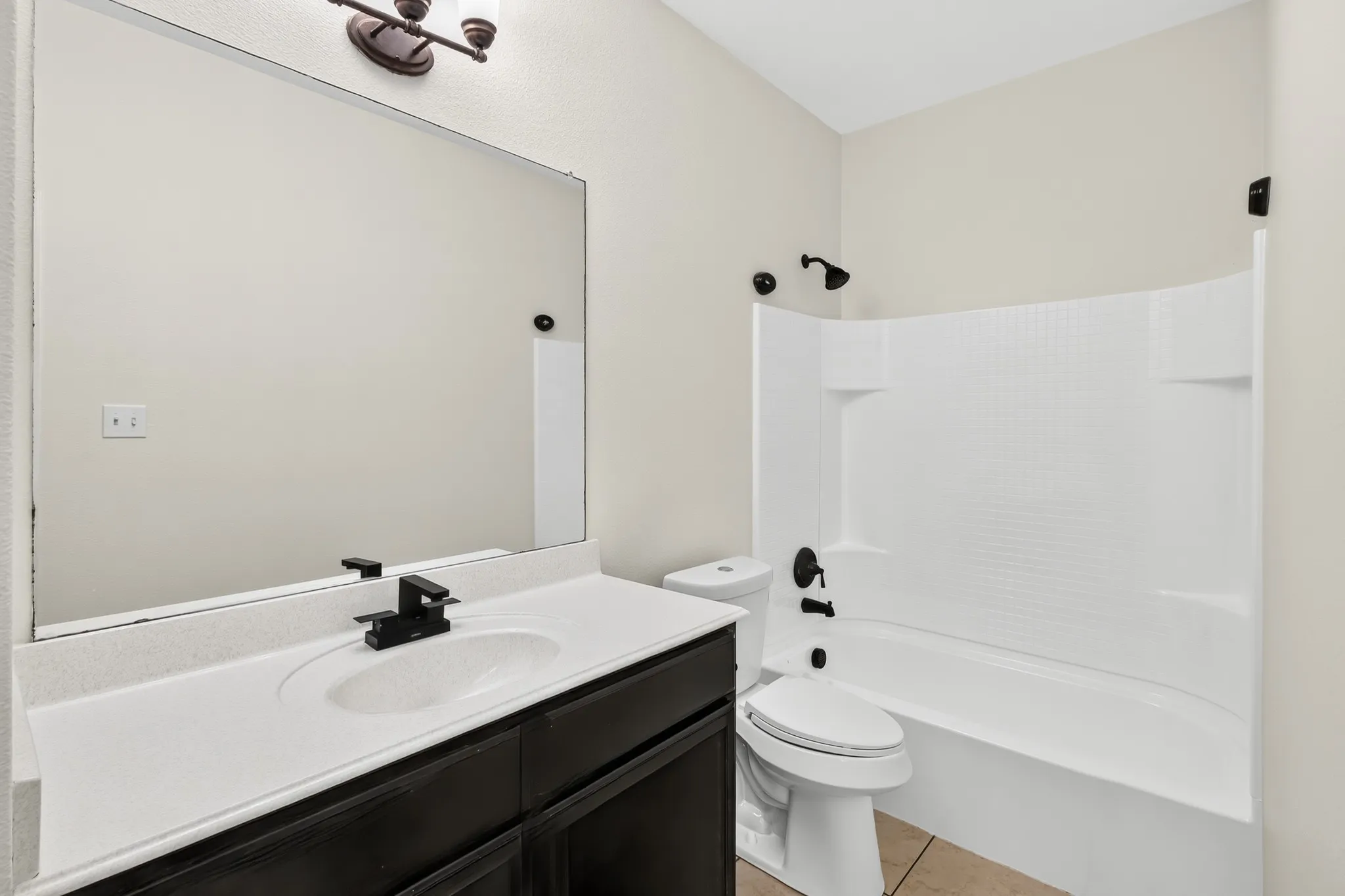Bathroom featuring a dark wood-finish vanity, white countertop with integrated sink, black-finish faucet, and a combination tub/shower with black-finish fixtures