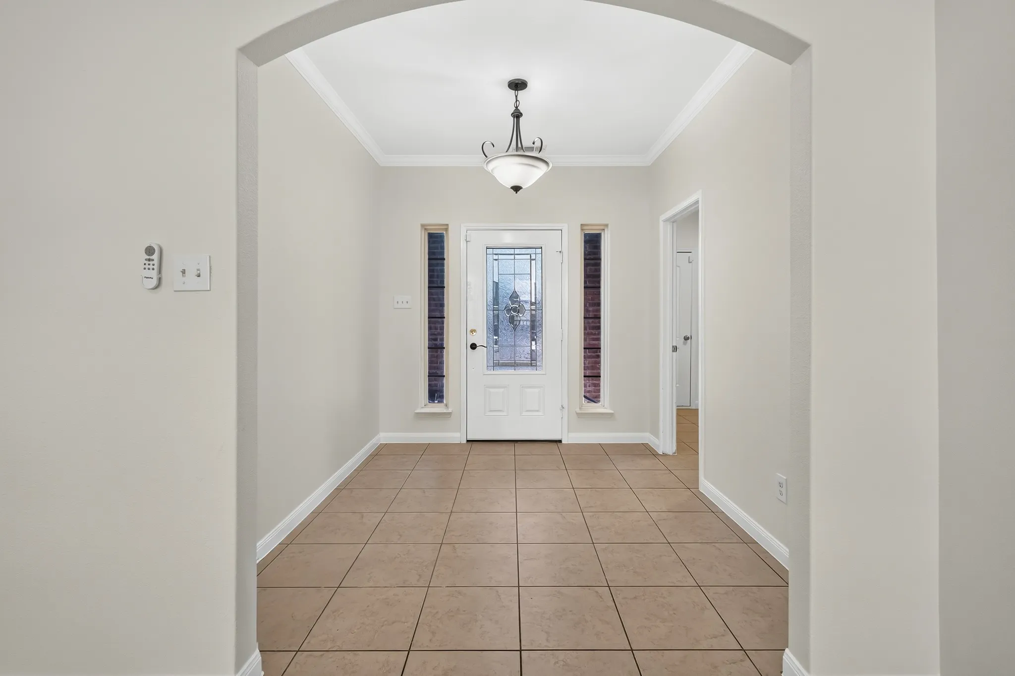 Arched doorway entry with tile flooring, crown molding, a decorative chandelier, and a front door with leaded glass