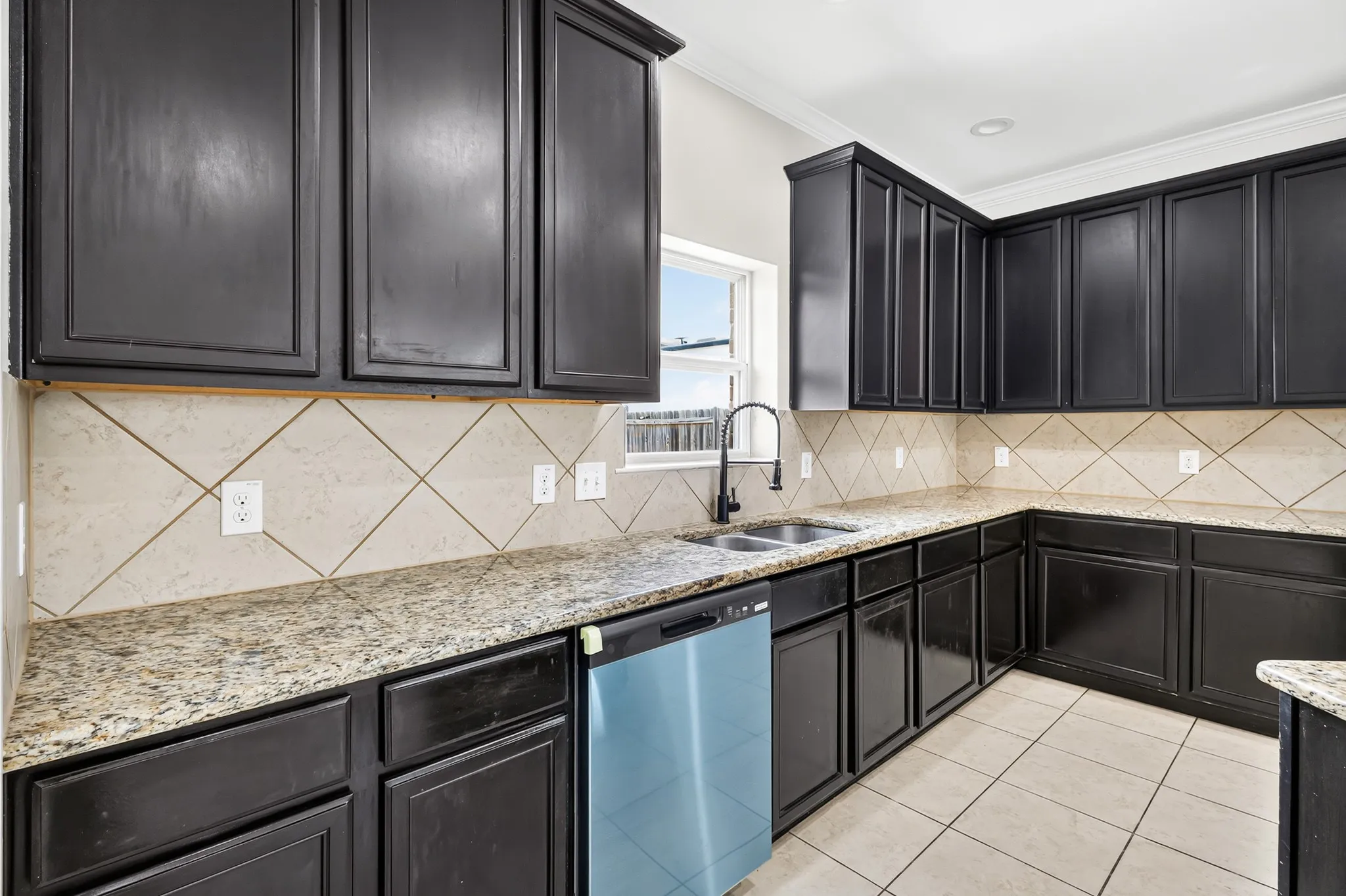 Contemporary kitchen featuring dark cabinetry, granite countertops, a tile backsplash, and a double basin sink with a modern faucet