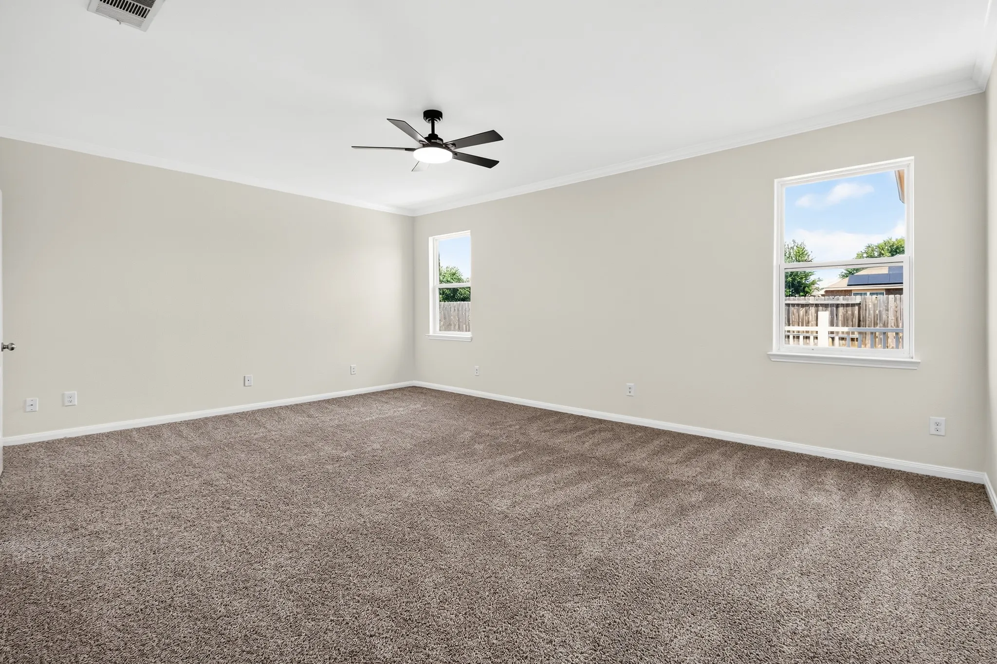 Spacious room with plush carpeting, two windows, crown molding, and a ceiling fan