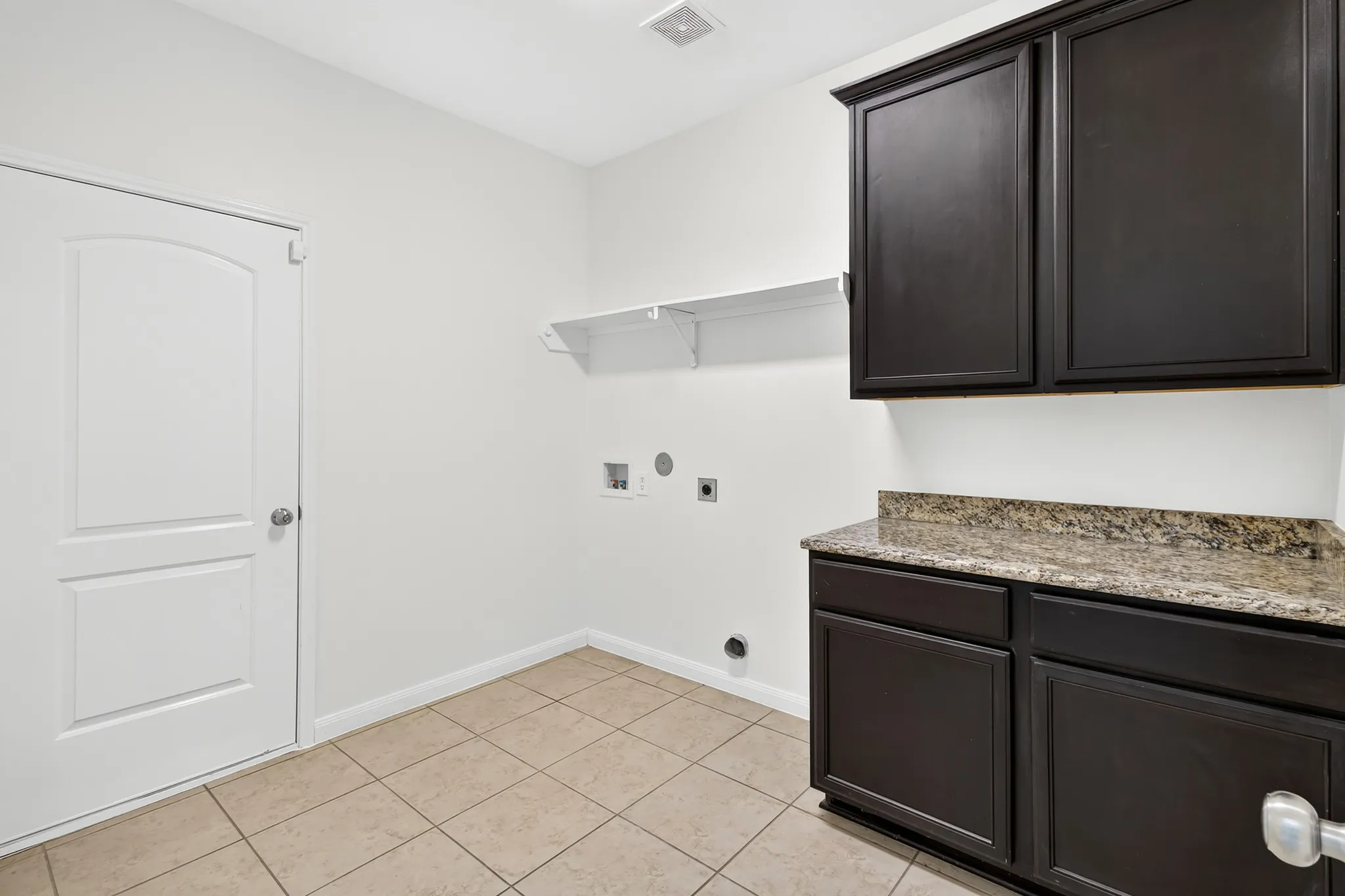 Tile flooring, dark wood-finish cabinetry, light-toned countertop, and wall-mounted shelving