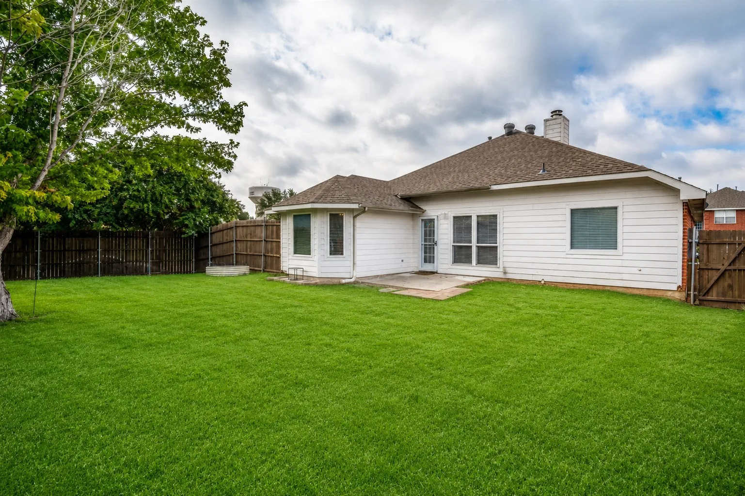 Expansive green lawn with mature trees, a privacy fence, and a concrete patio