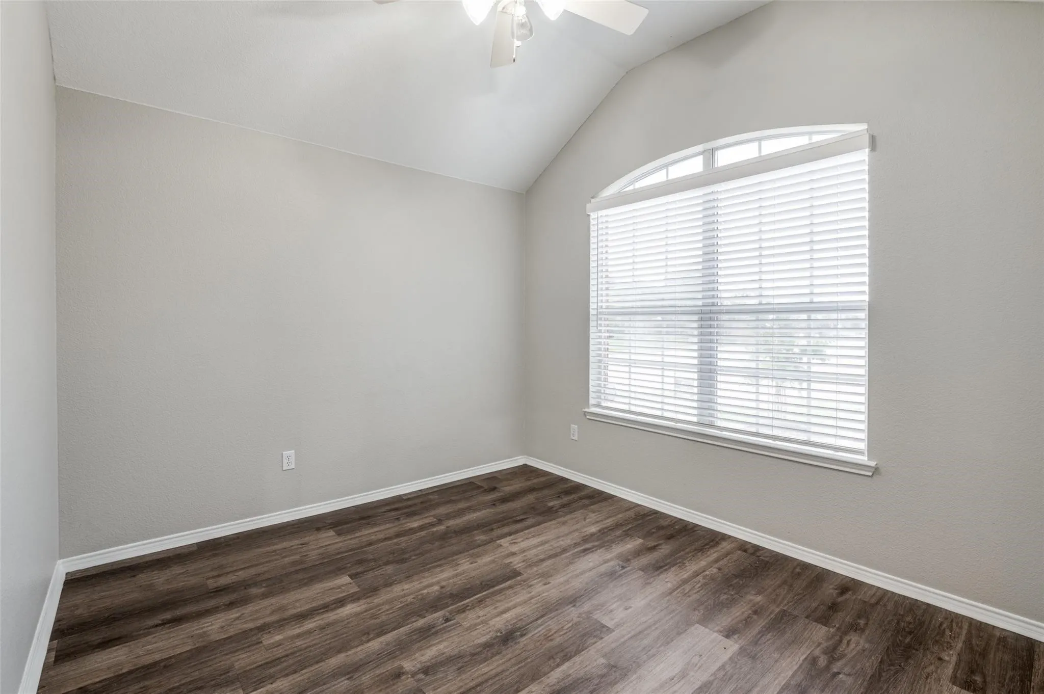 Vaulted ceiling with a ceiling fan, arched window with blinds, and wood-finish flooring