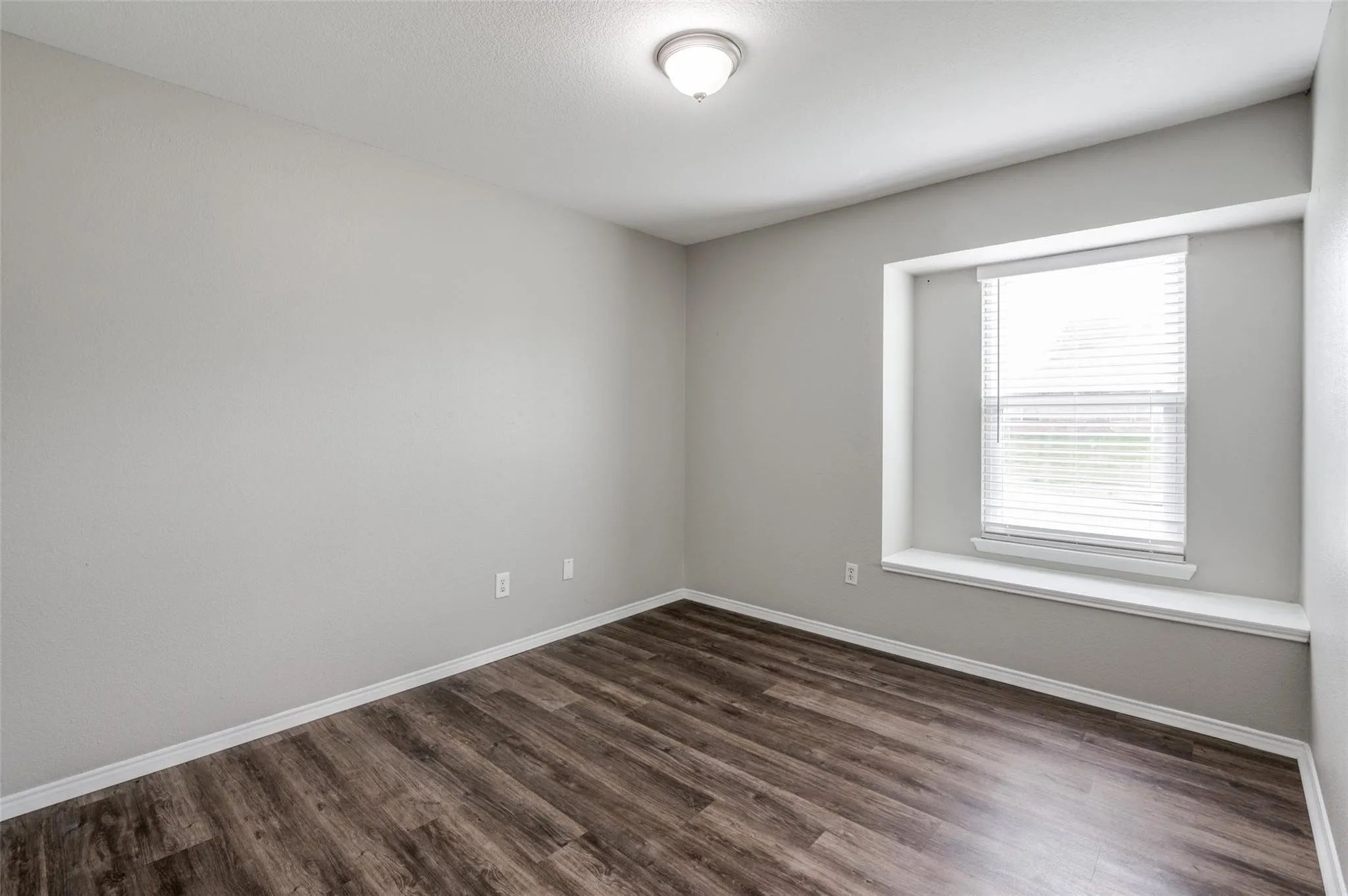 Wood-finish flooring, light gray walls, white trim, and a window with white blinds and a deep sill
