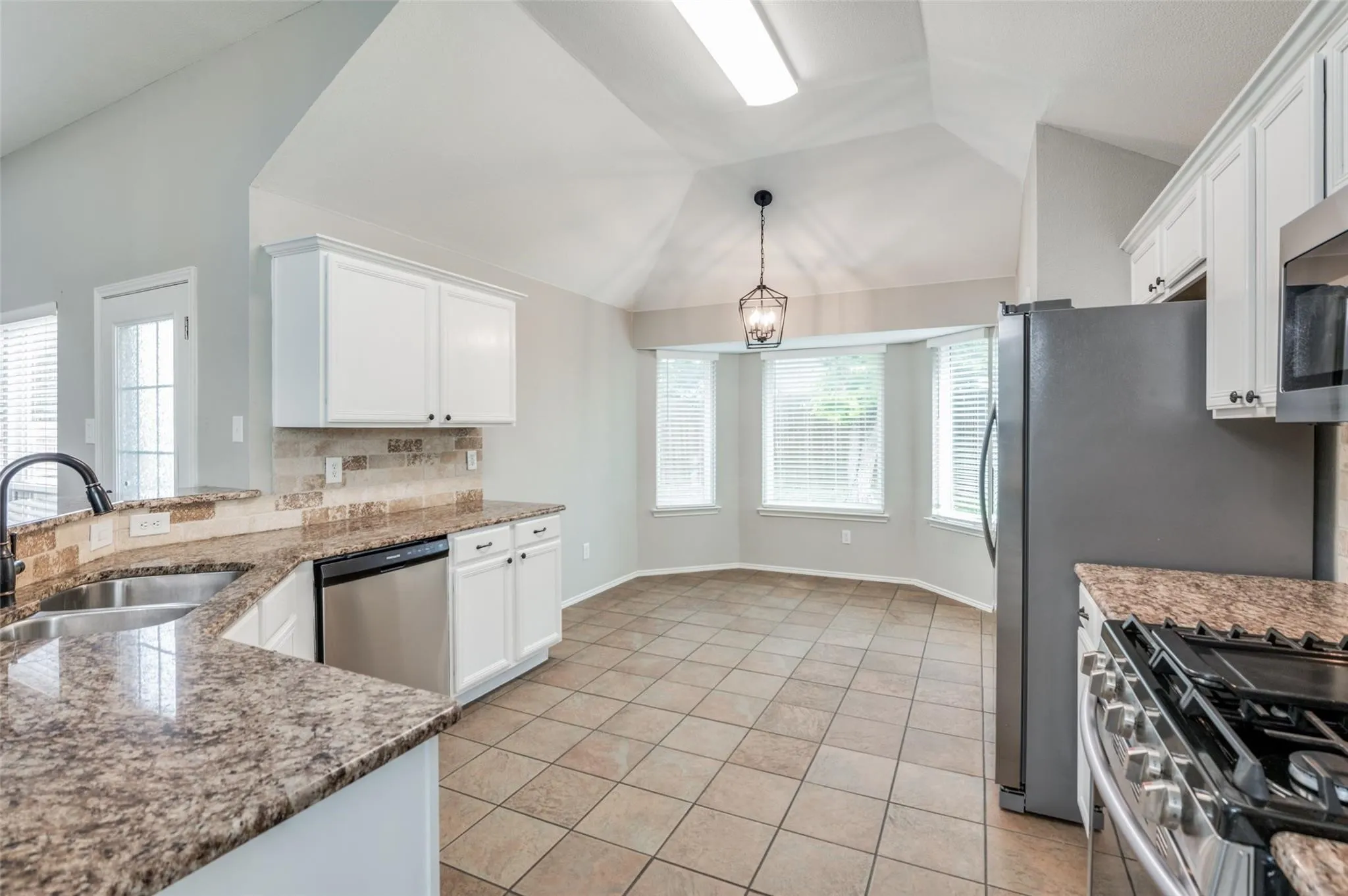 Kitchen featuring white cabinetry, stainless steel appliances, granite countertops, and a tiled backsplash