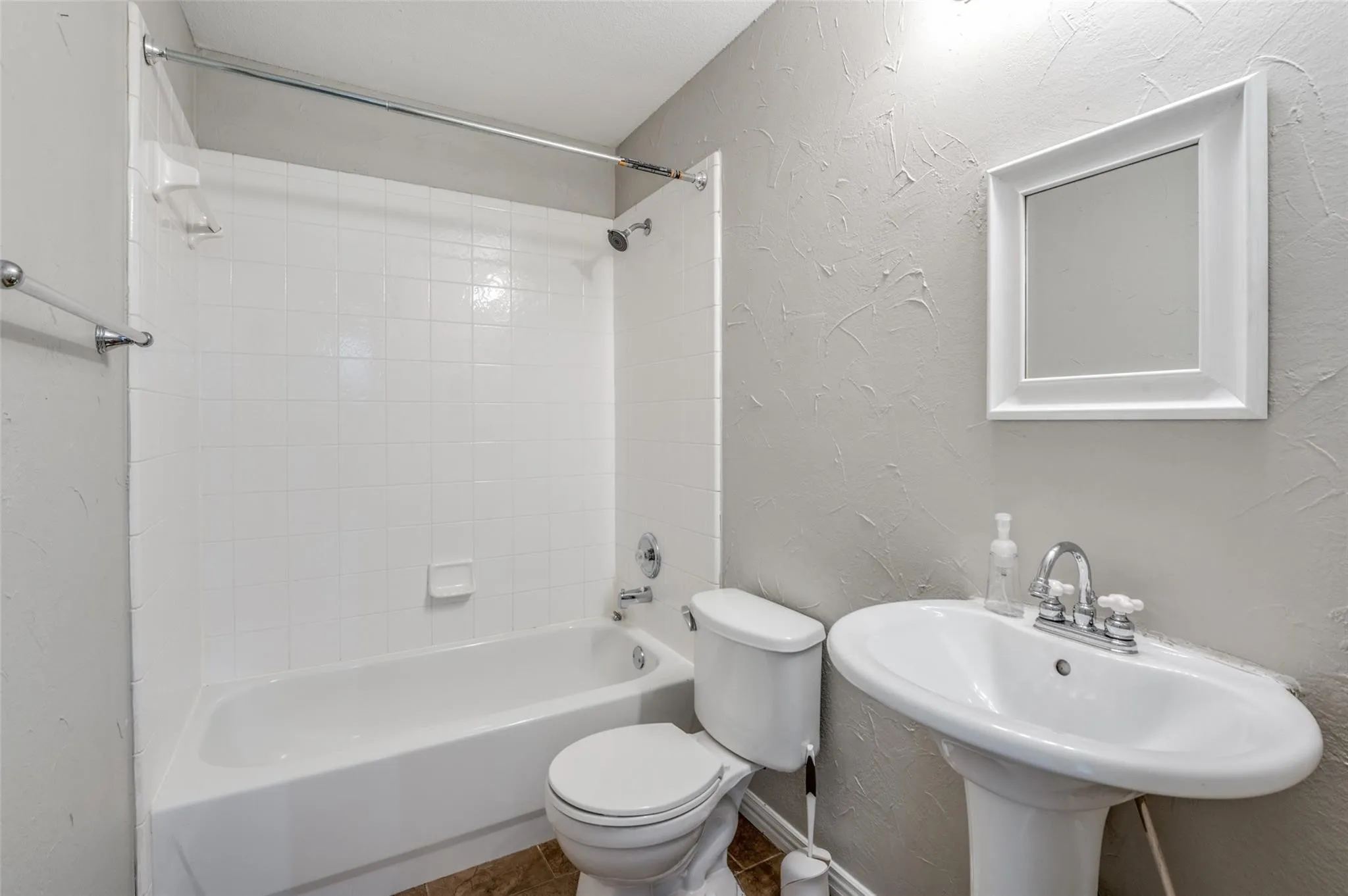 White pedestal sink with chrome faucet, a white-framed mirror, and a white tub with tile surround