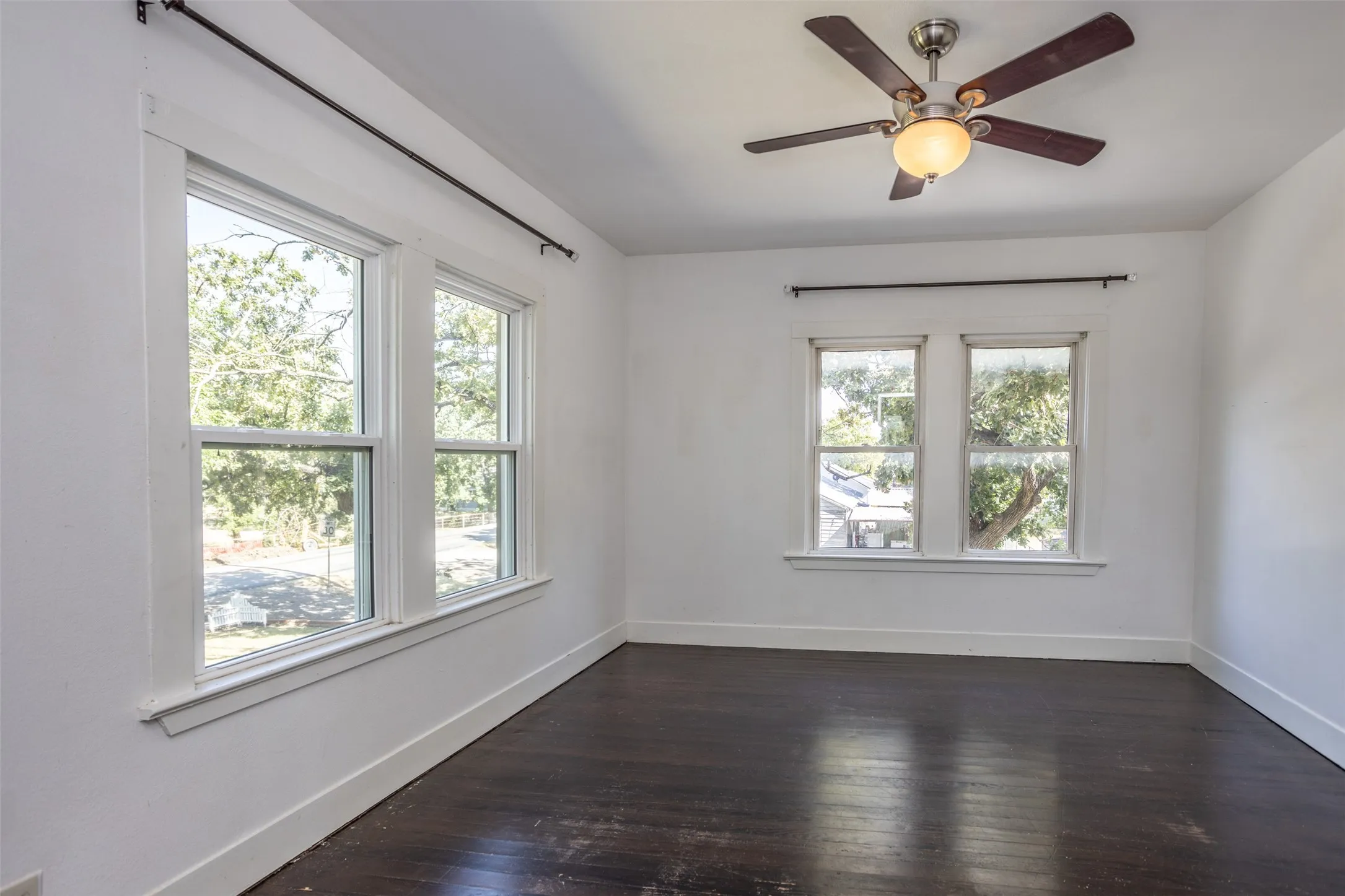 Dark-finish flooring, multiple windows with white trim, and a ceiling fan with light fixture