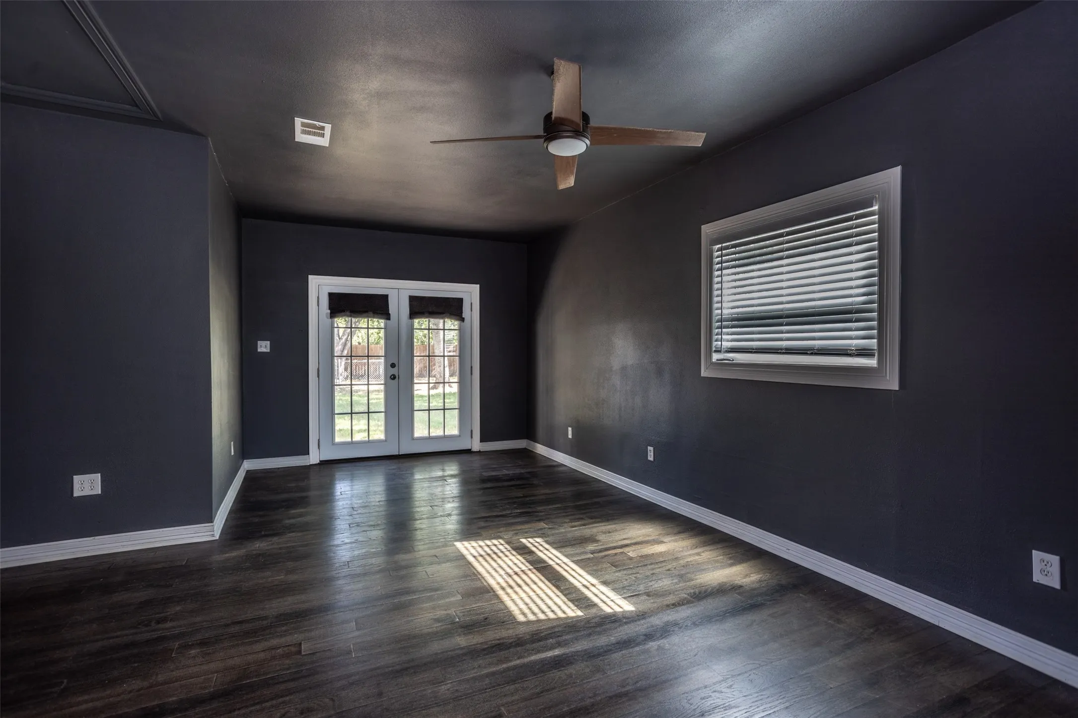 Wood-finish flooring, white trim, ceiling fan, window with blinds, and white French doors