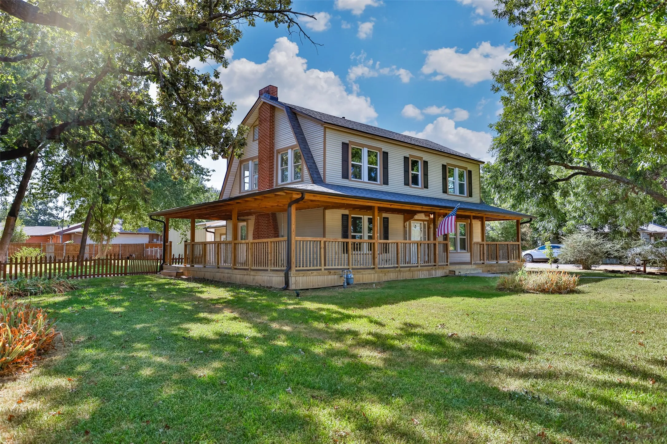 Two-story residence featuring a full-width covered porch with wood railings, a prominent brick chimney, and a gambrel roofline