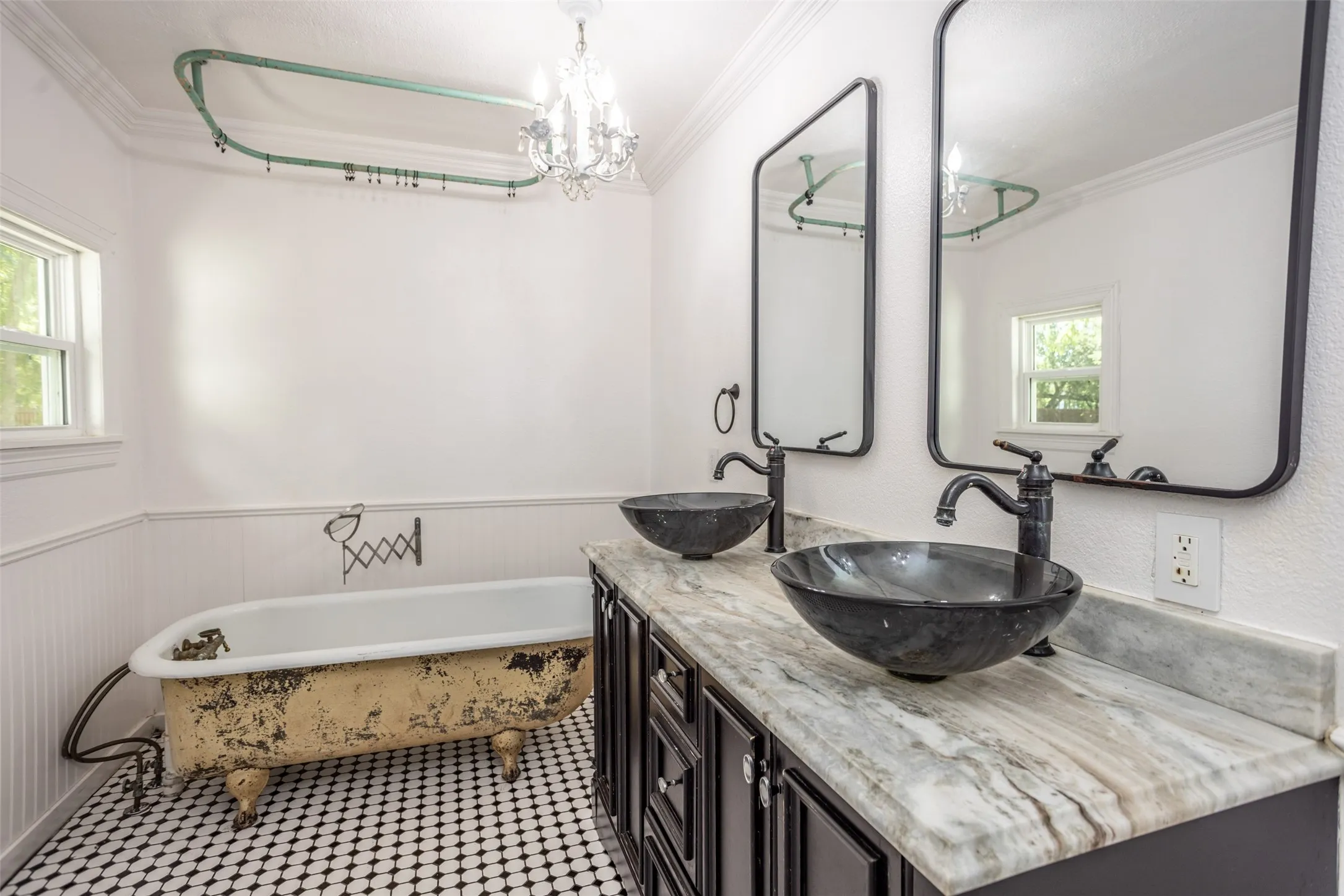 Dual vessel sinks with dark bronze fixtures, a stone countertop, black framed mirrors, and a clawfoot tub