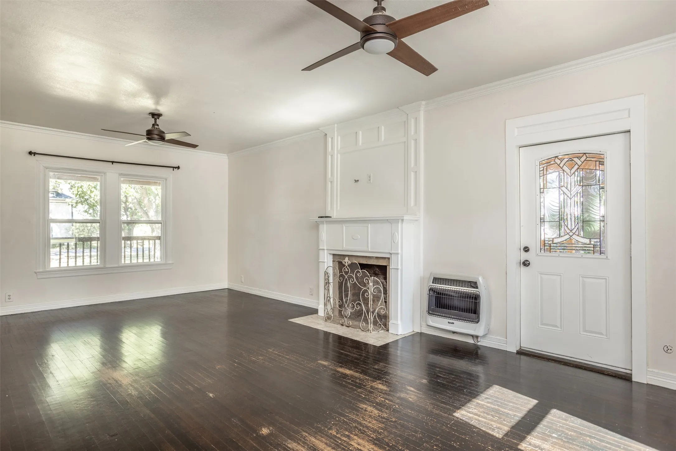 Hardwood flooring throughout, featuring a decorative fireplace with an ornate metal screen, and a stained glass detail entry door