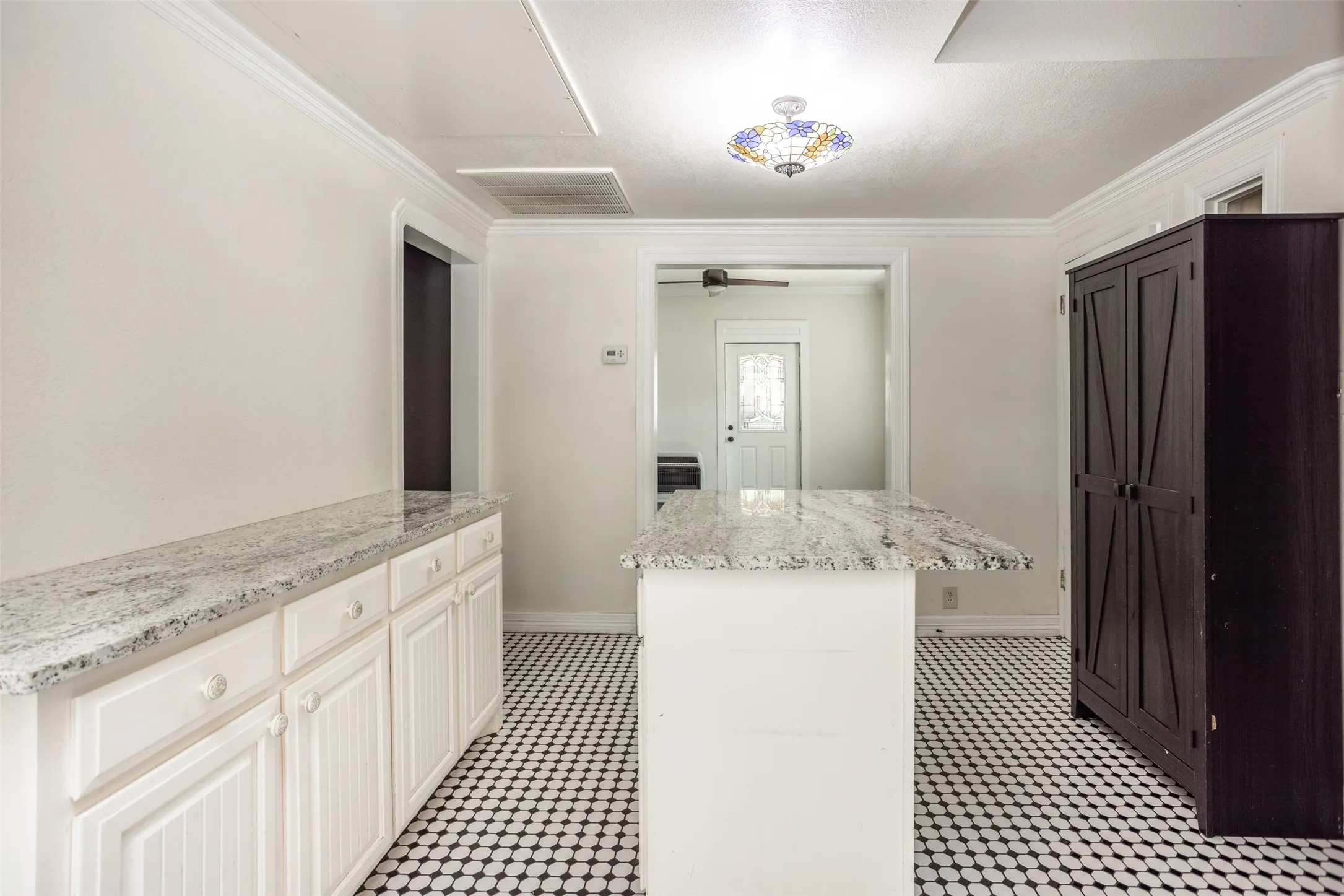 White cabinetry with paneling, patterned tile flooring, stone countertops, crown molding, and a decorative ceiling light fixture