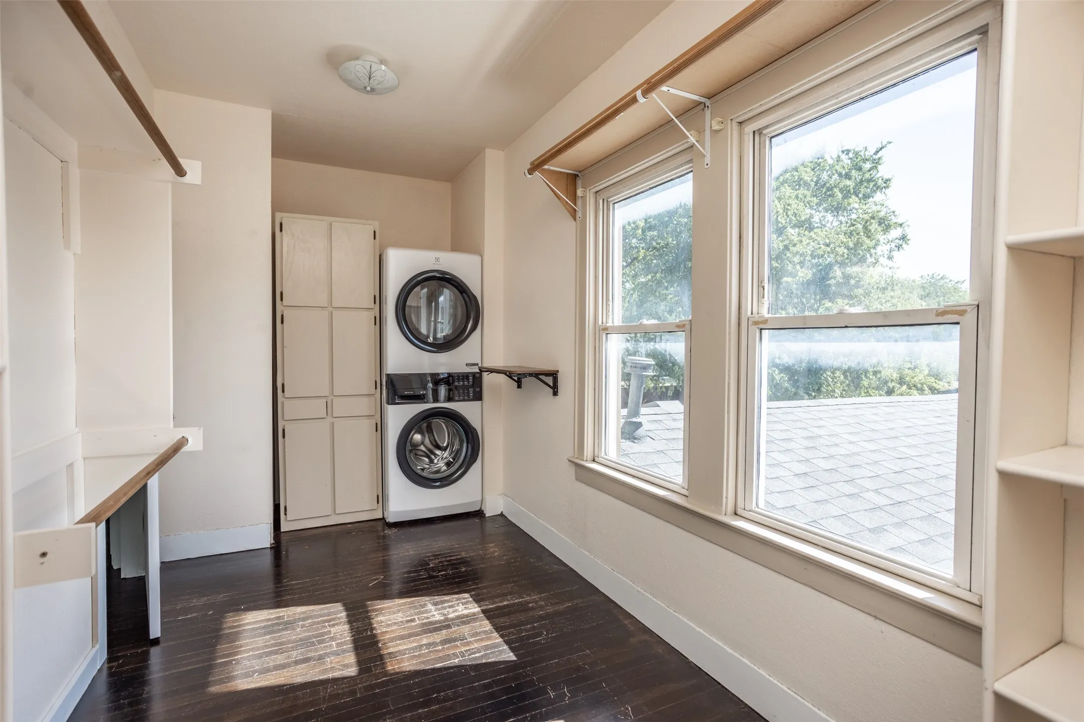 Laundry area featuring built-in cabinetry, dark wood-finish flooring, and a stacked washer and dryer