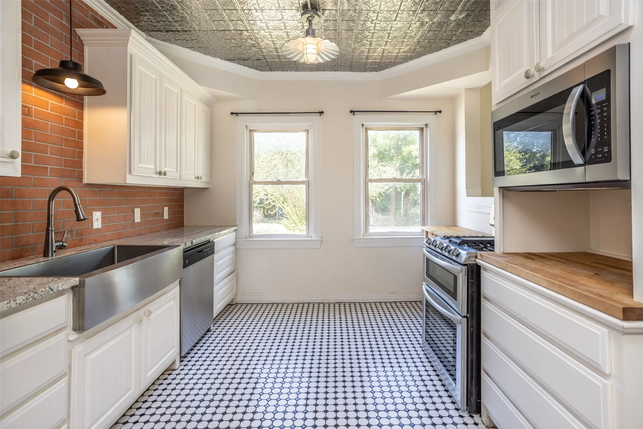 Kitchen featuring white cabinetry, black and white hexagonal tile flooring, a stainless steel farm sink, a brick-style backsplash, and a tin ceiling