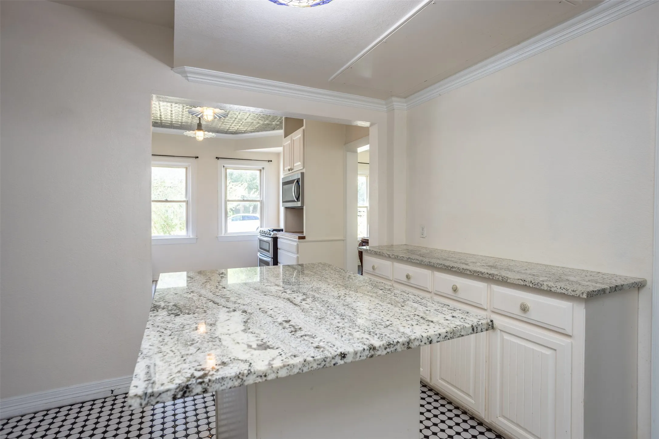 Granite countertops, white cabinetry, integrated stainless steel microwave, stainless steel range, and black and white hexagonal floor tiling