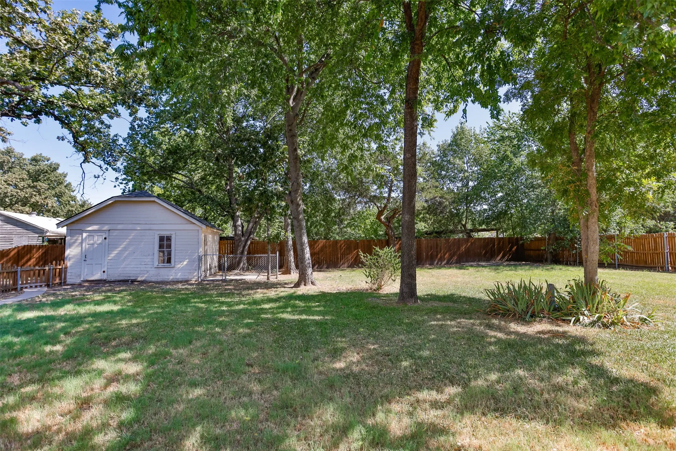 Storage and small garage Expansive lawn area, mature trees, wood privacy fencing, a separate white accessory building, and a picket fence