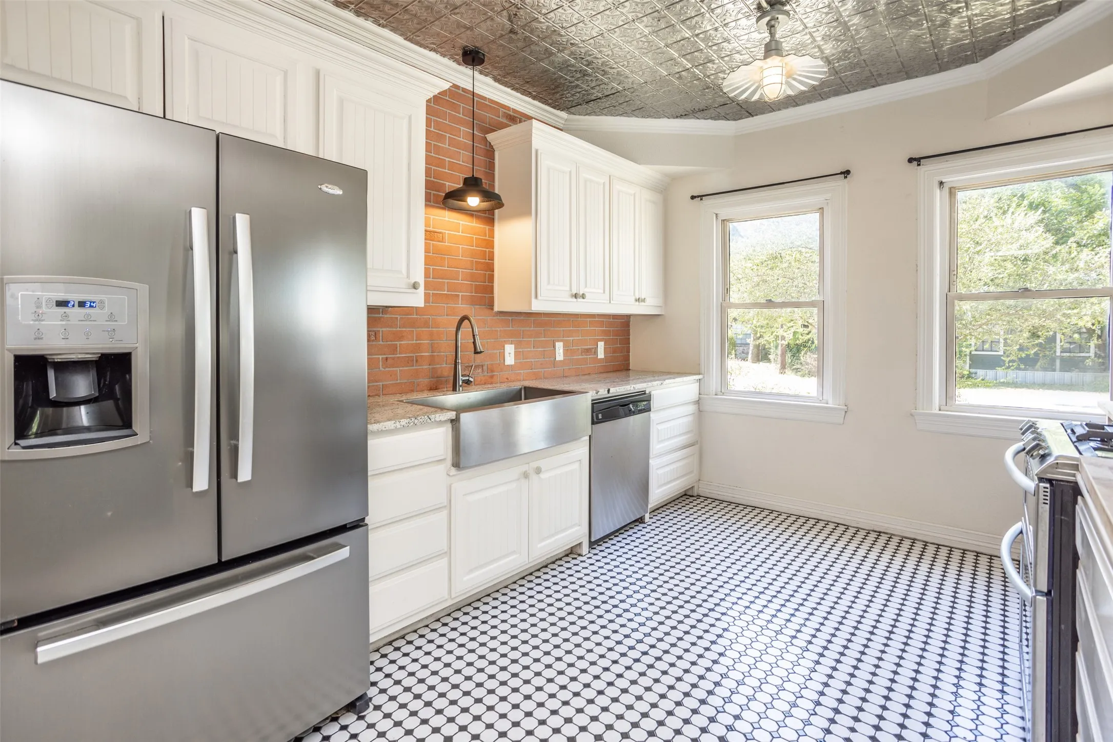Kitchen featuring black and white hexagonal tile flooring, white cabinetry, brick backsplash, stainless steel appliances, and a metal ceiling