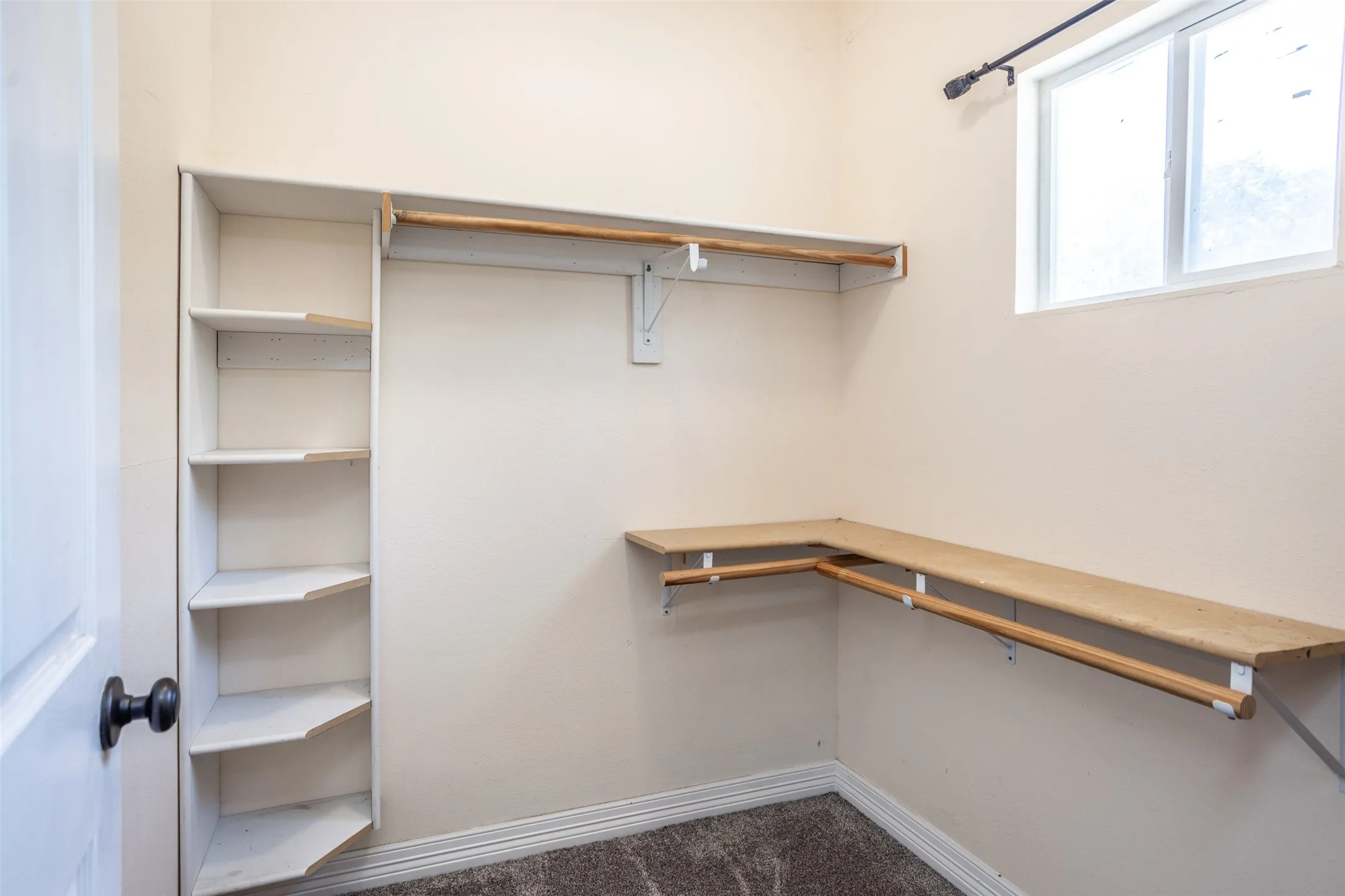 Built-in shelving, hanging rods, L-shaped shelving, a window, and carpet flooring