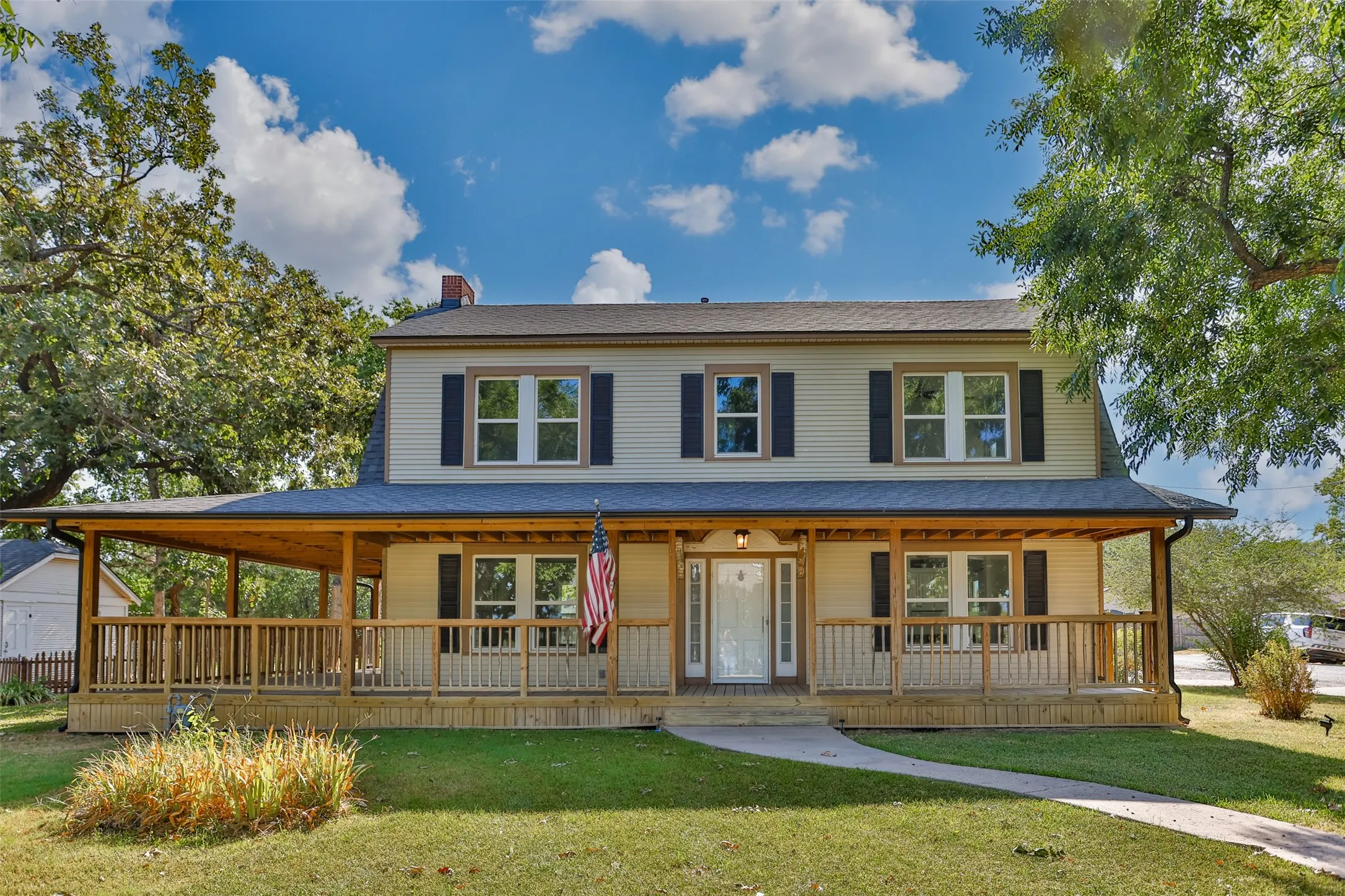 Two-story residence featuring light-colored siding, a full-width covered porch with wood railings, a gray shingle roof, and multiple windows with dark shutters
