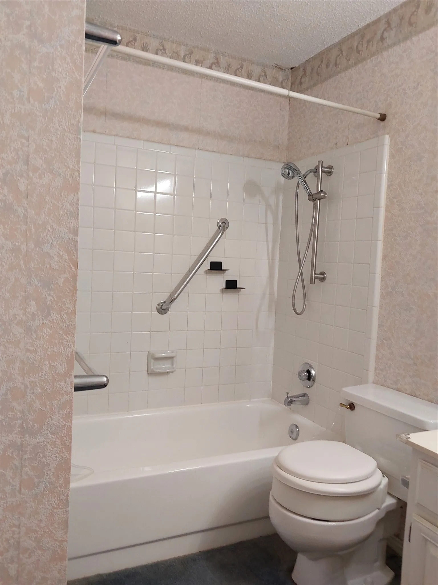 Bathtub with white tile surround, chrome fixtures, and grab bars