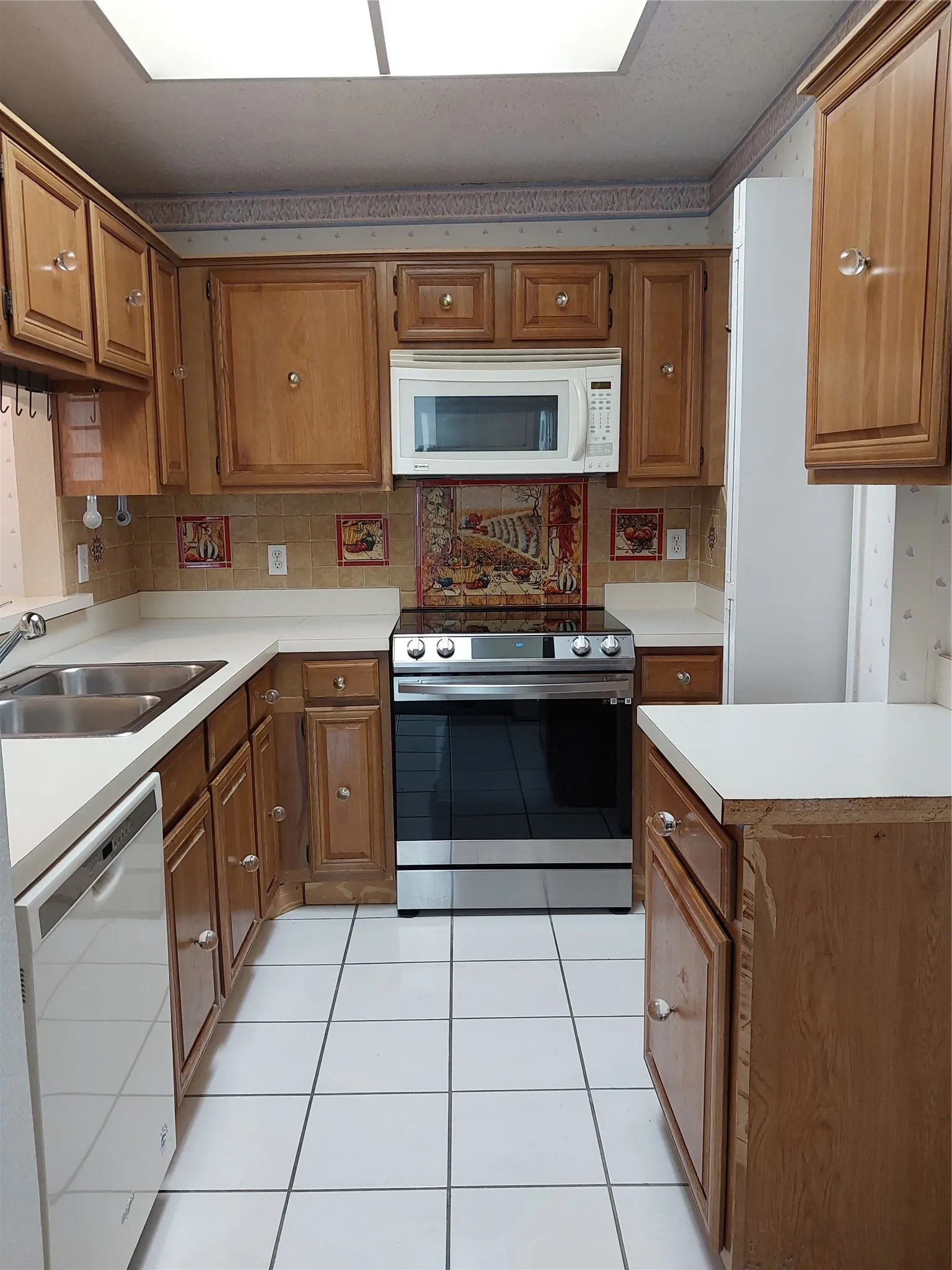 Wood-finish cabinetry with clear knob hardware, white tile flooring, double basin sink, and stainless steel range