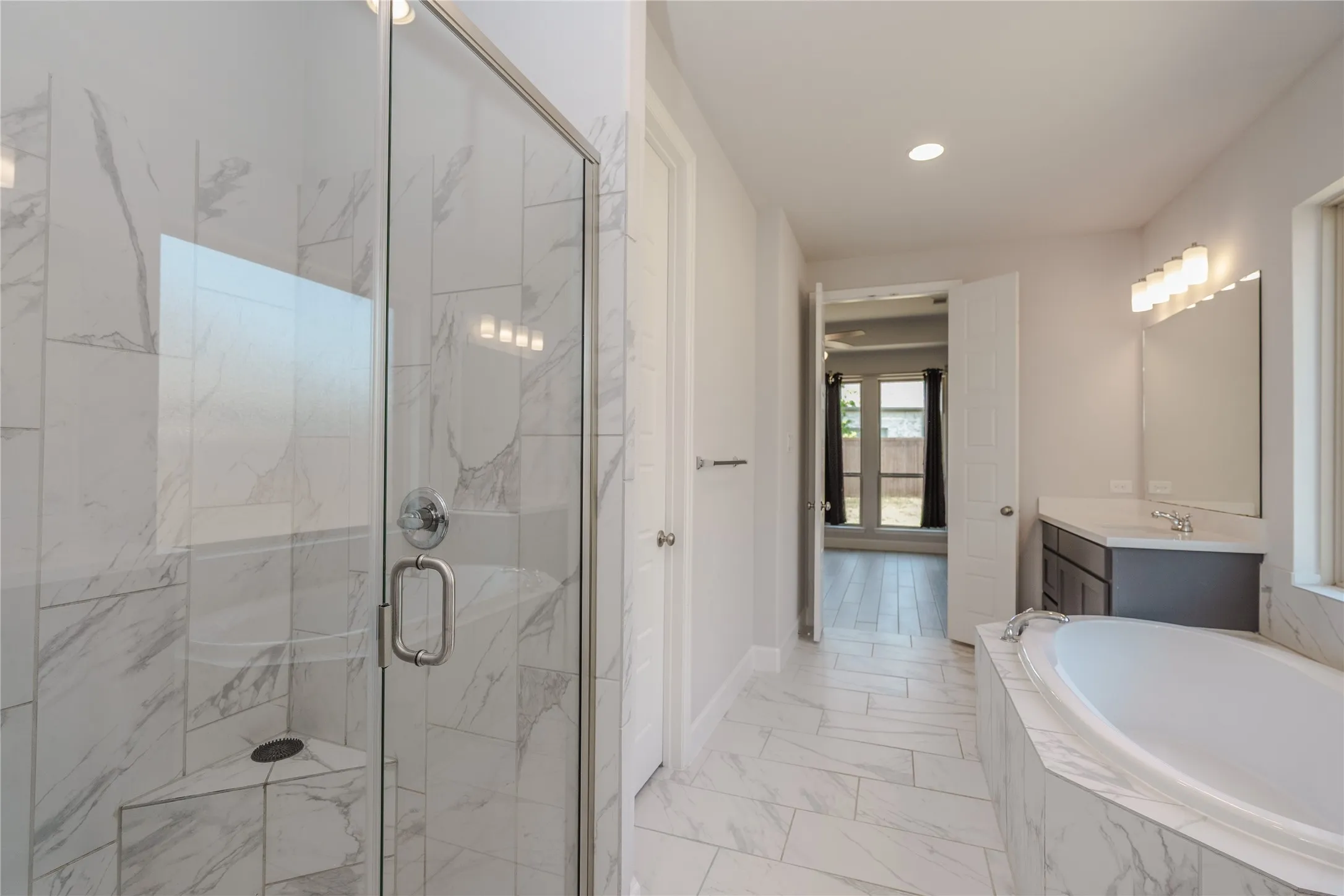 Frameless glass shower enclosure, built-in soaking tub, large vanity with countertop, and modern lighting fixture
