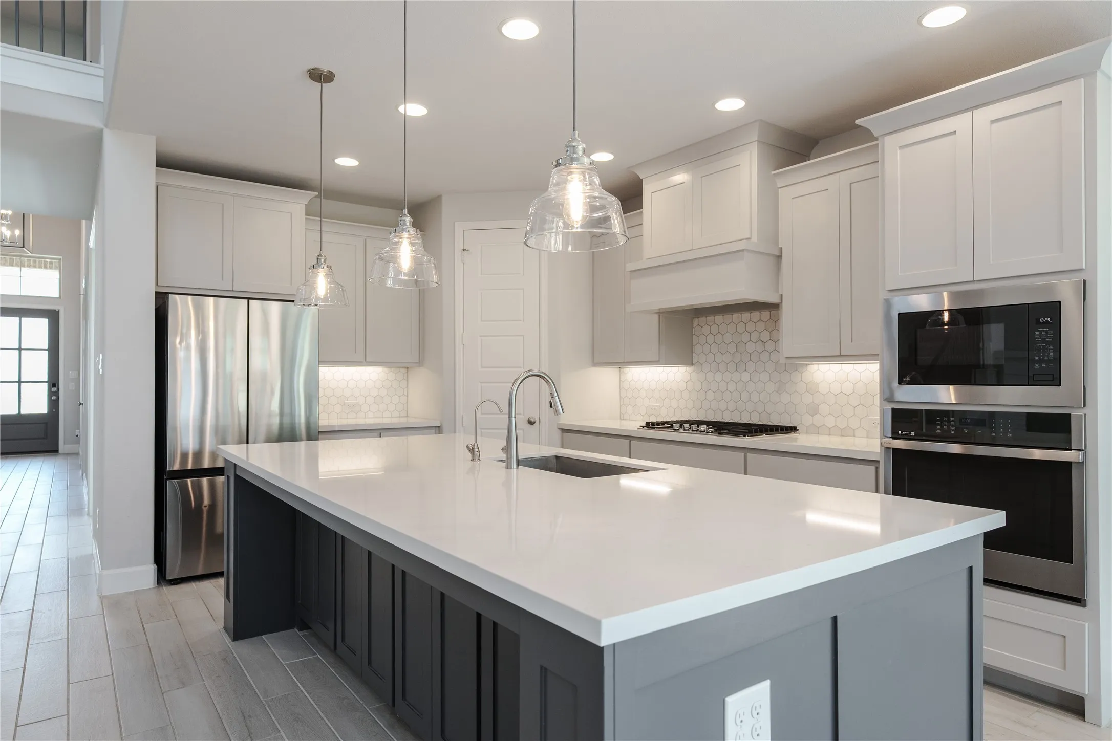 Expansive kitchen island with a light-colored countertop, stainless steel appliances, light wood-finish flooring, recessed lighting, and pendant lighting fixtures