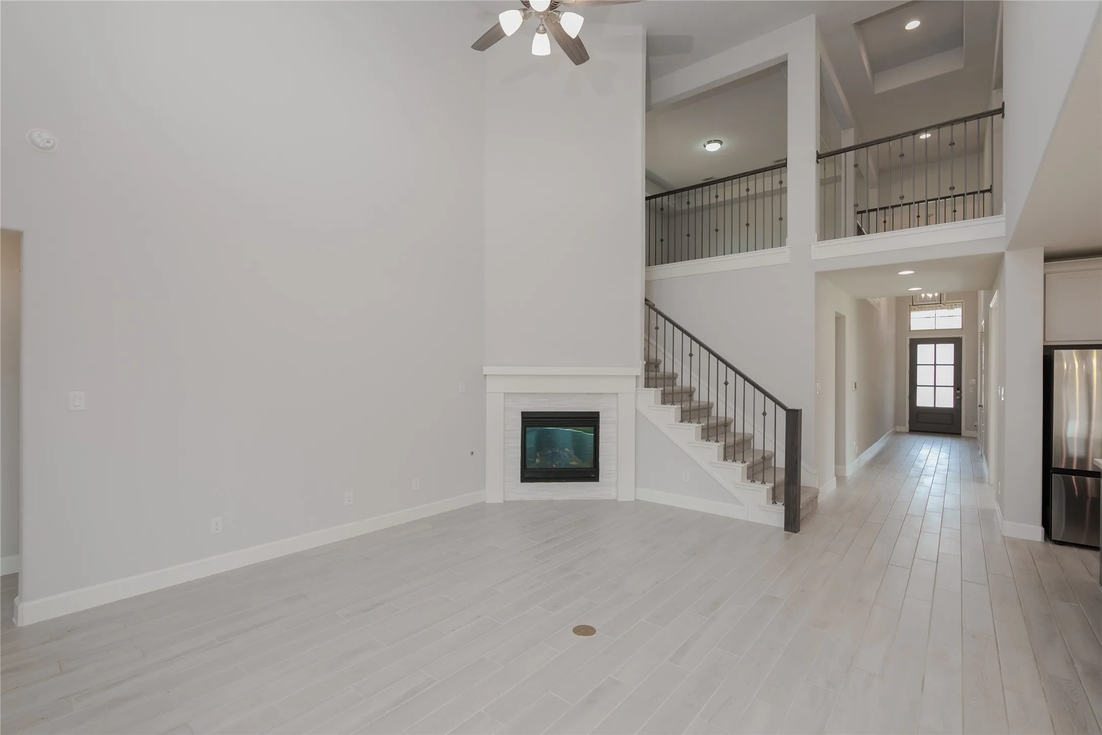 Two-story living area with wood-look flooring, a corner fireplace with a white mantel, and a staircase with dark iron balusters