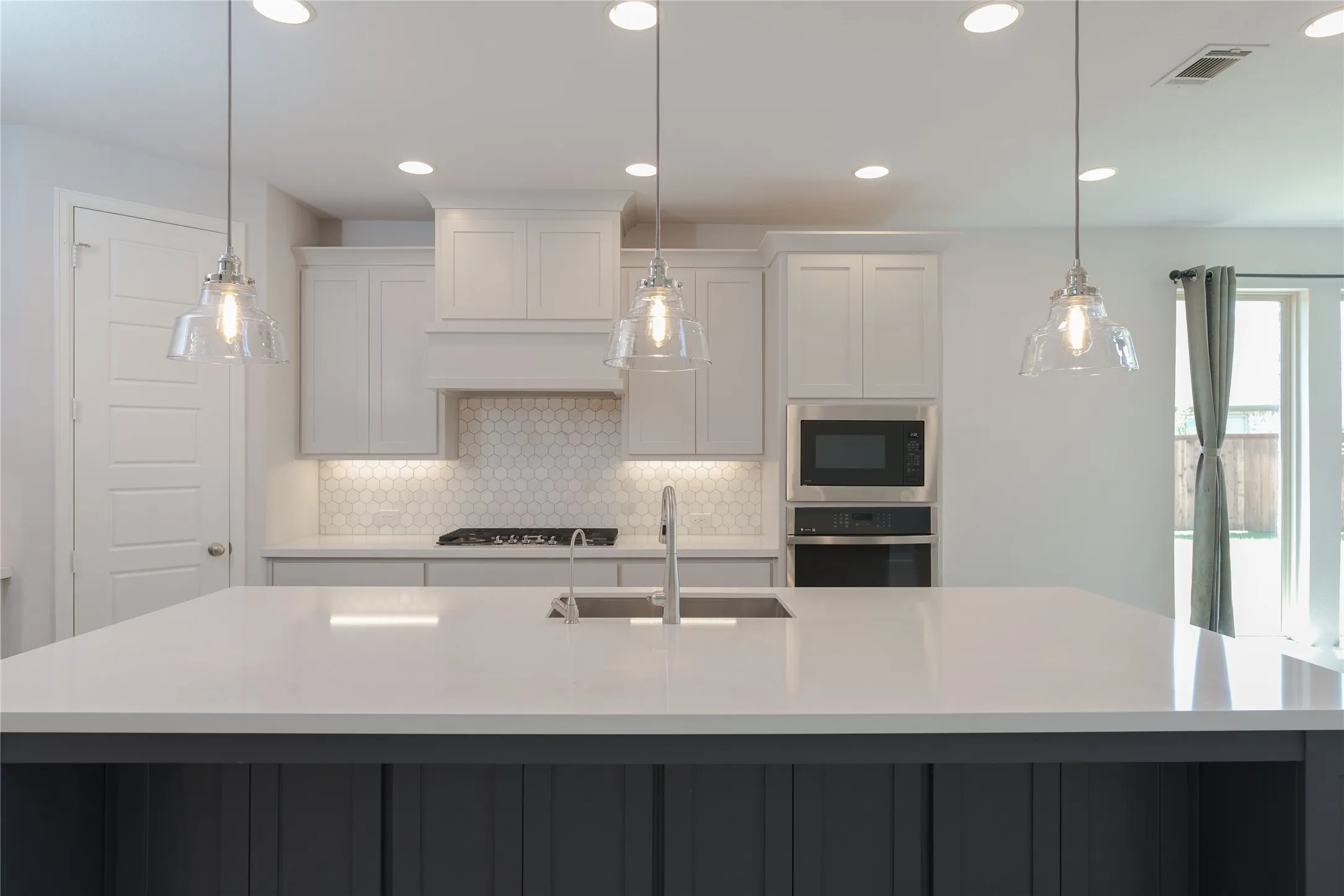 Expansive kitchen island with a light-toned countertop, stainless steel sink, and pendant lighting
