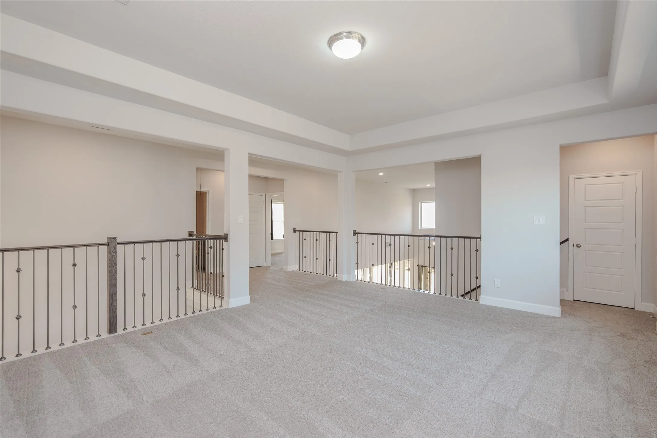Spacious open loft area with coffered ceiling, plush carpeting, and wrought iron balusters