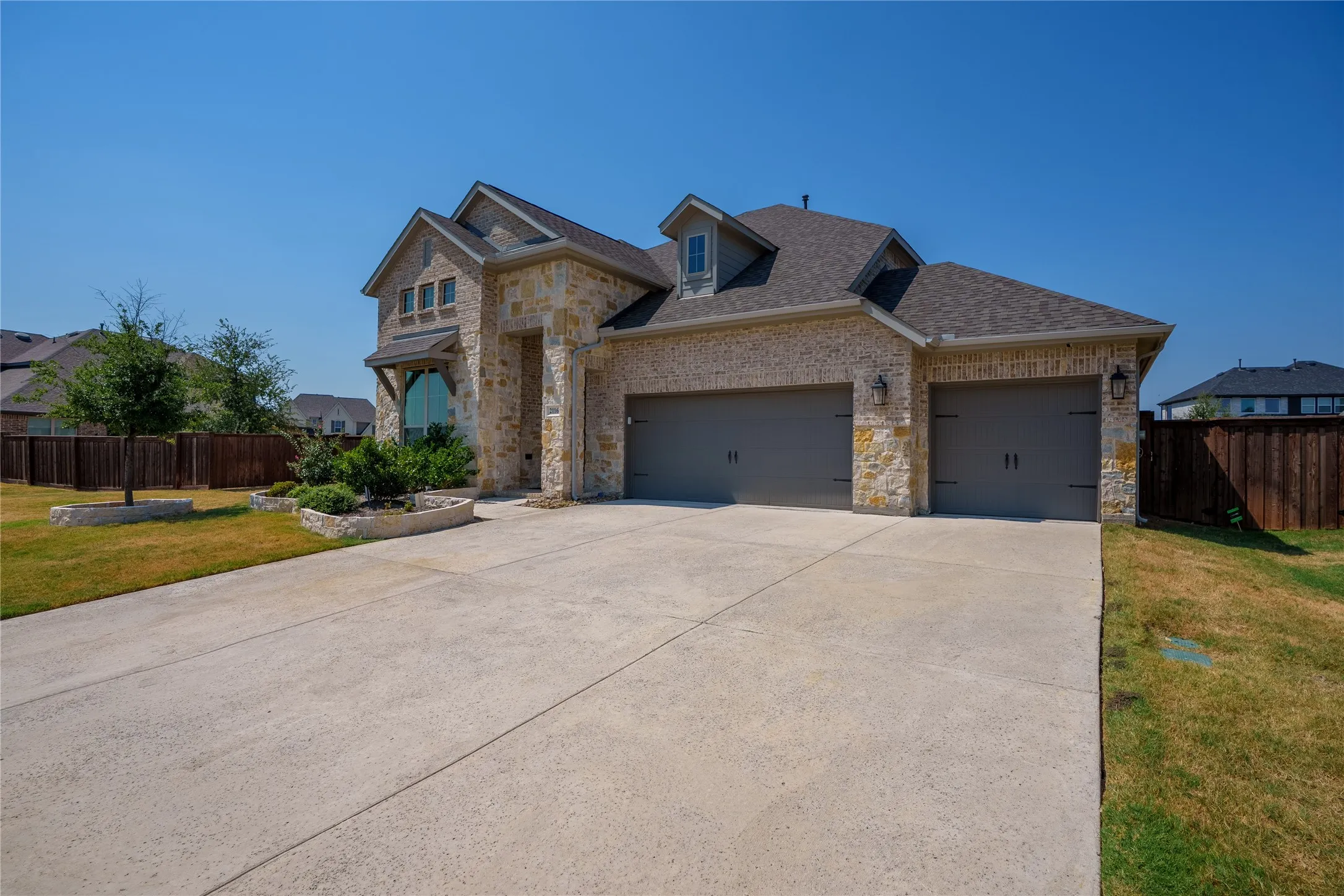 Stone and brick facade with a two-car garage, dormer window, and arched window