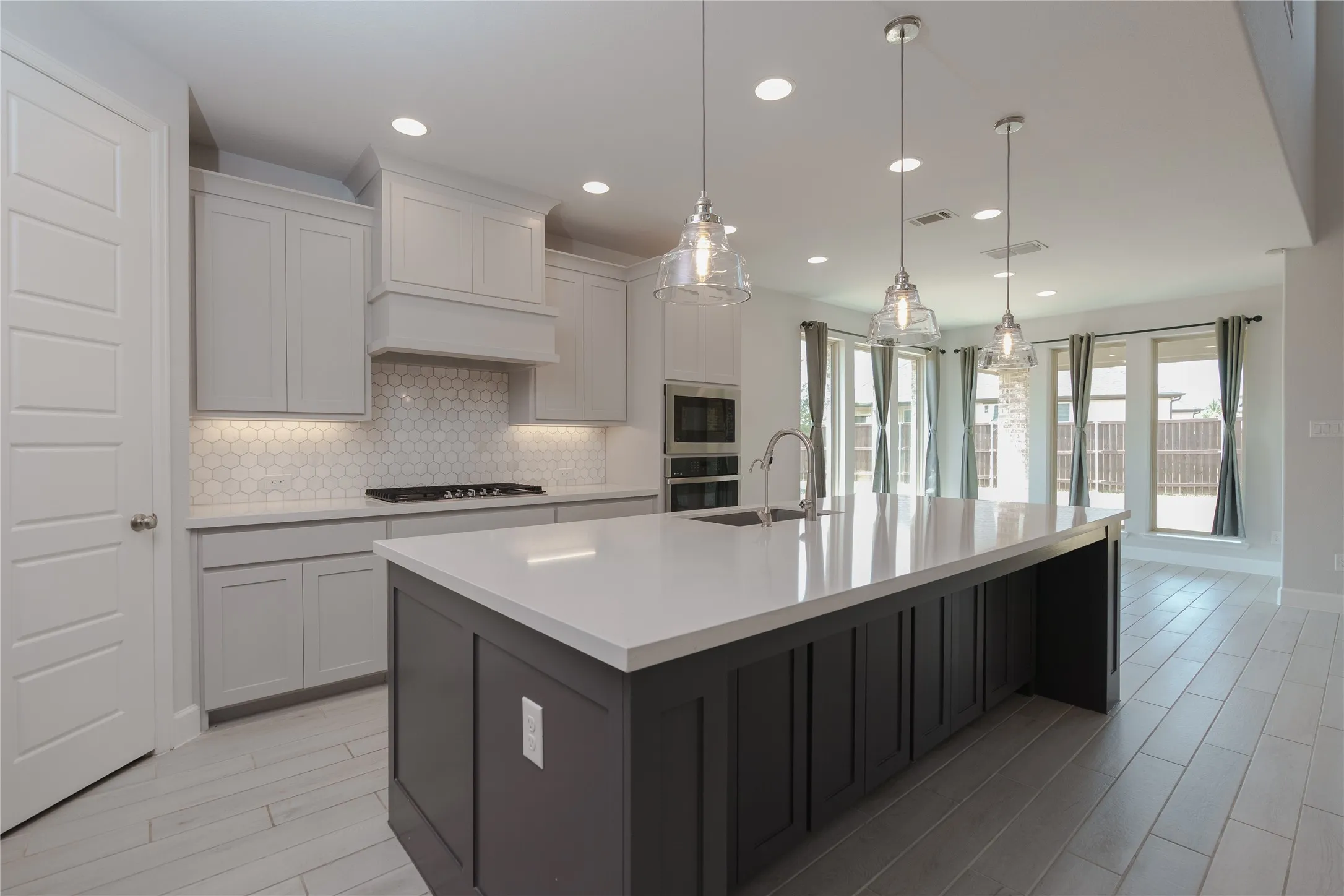Open-concept kitchen with a large island, pendant lighting, built-in stainless steel appliances, light wood-finish flooring, and a tiled backsplash