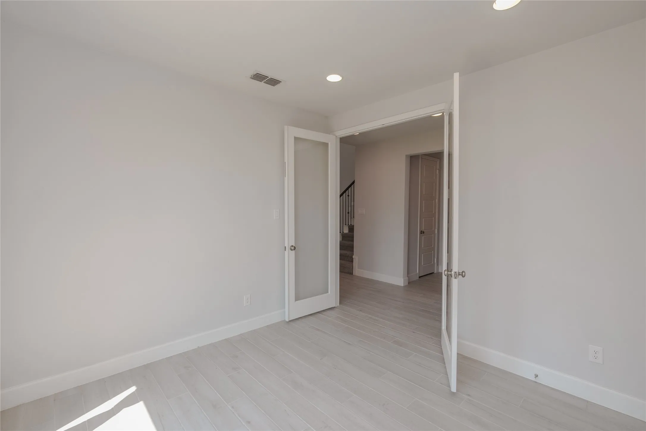 Recessed lighting, light-toned wood-finish flooring, white walls, and French doors with frosted glass panels