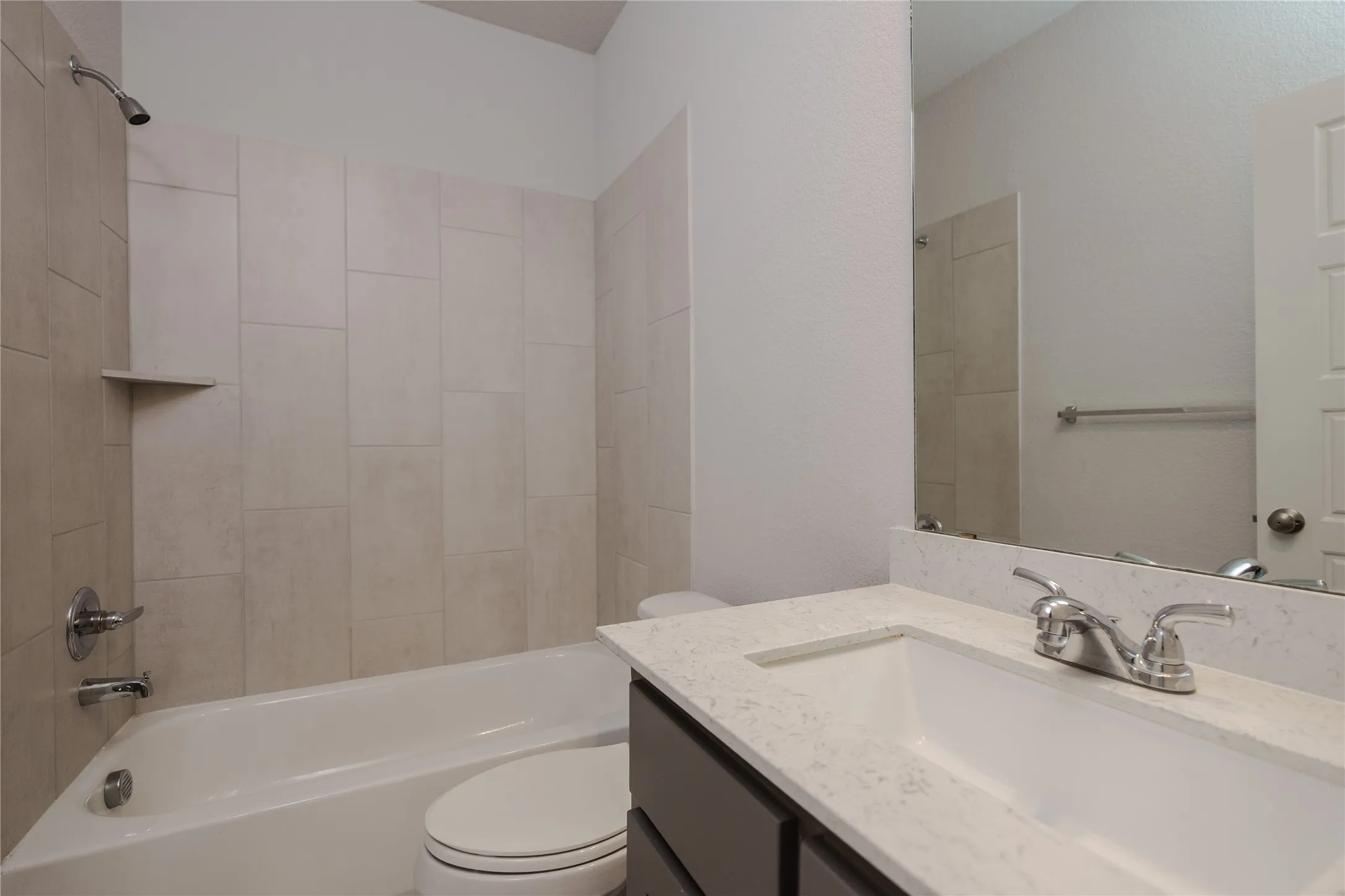 Bathroom featuring a built-in bathtub, a tiled shower surround with an integrated shelf, a vanity with a light-colored countertop, and a large wall-mounted mirror