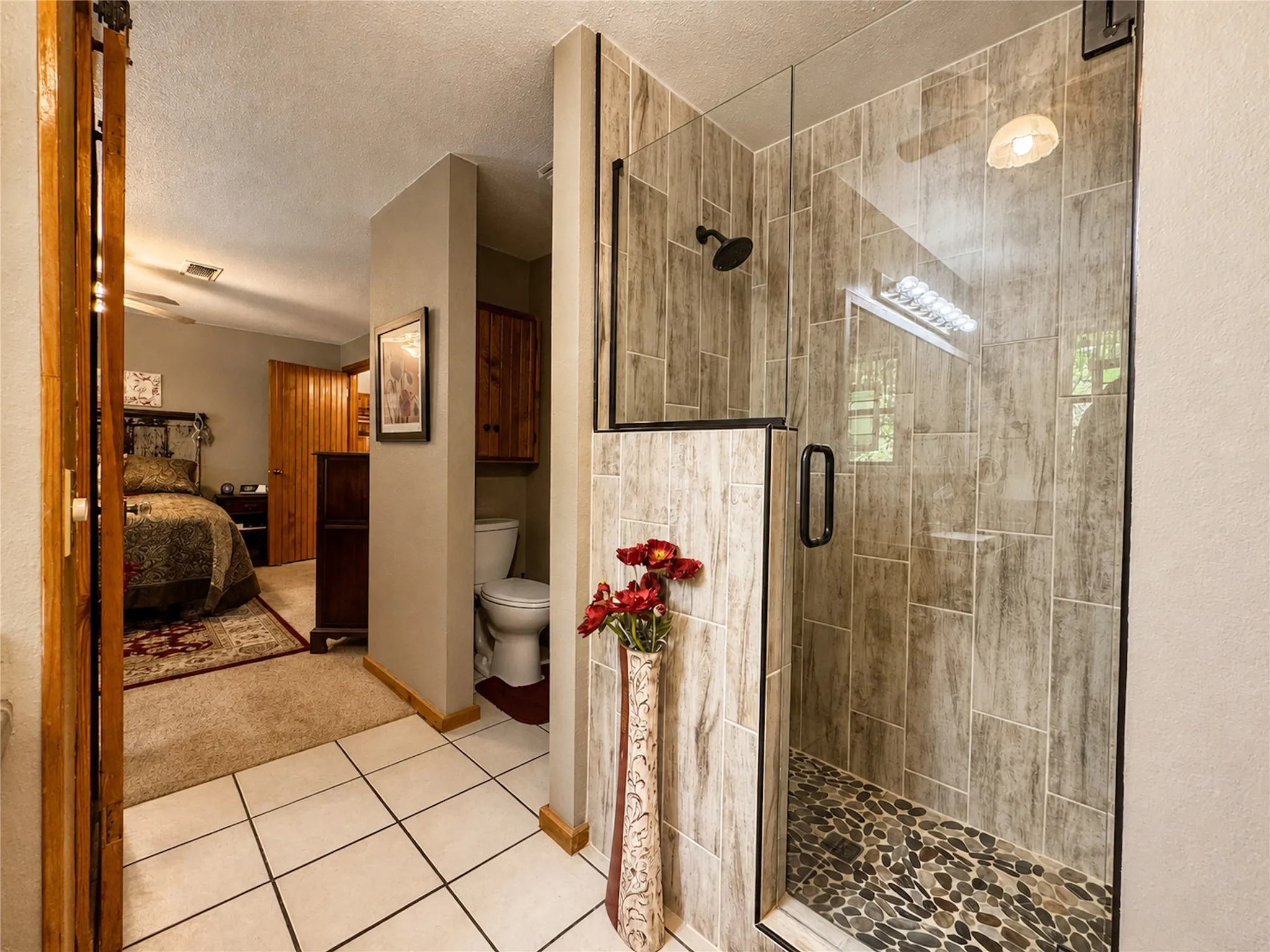 Walk-in shower with clear glass enclosure, stone tile walls, and a river rock shower floor