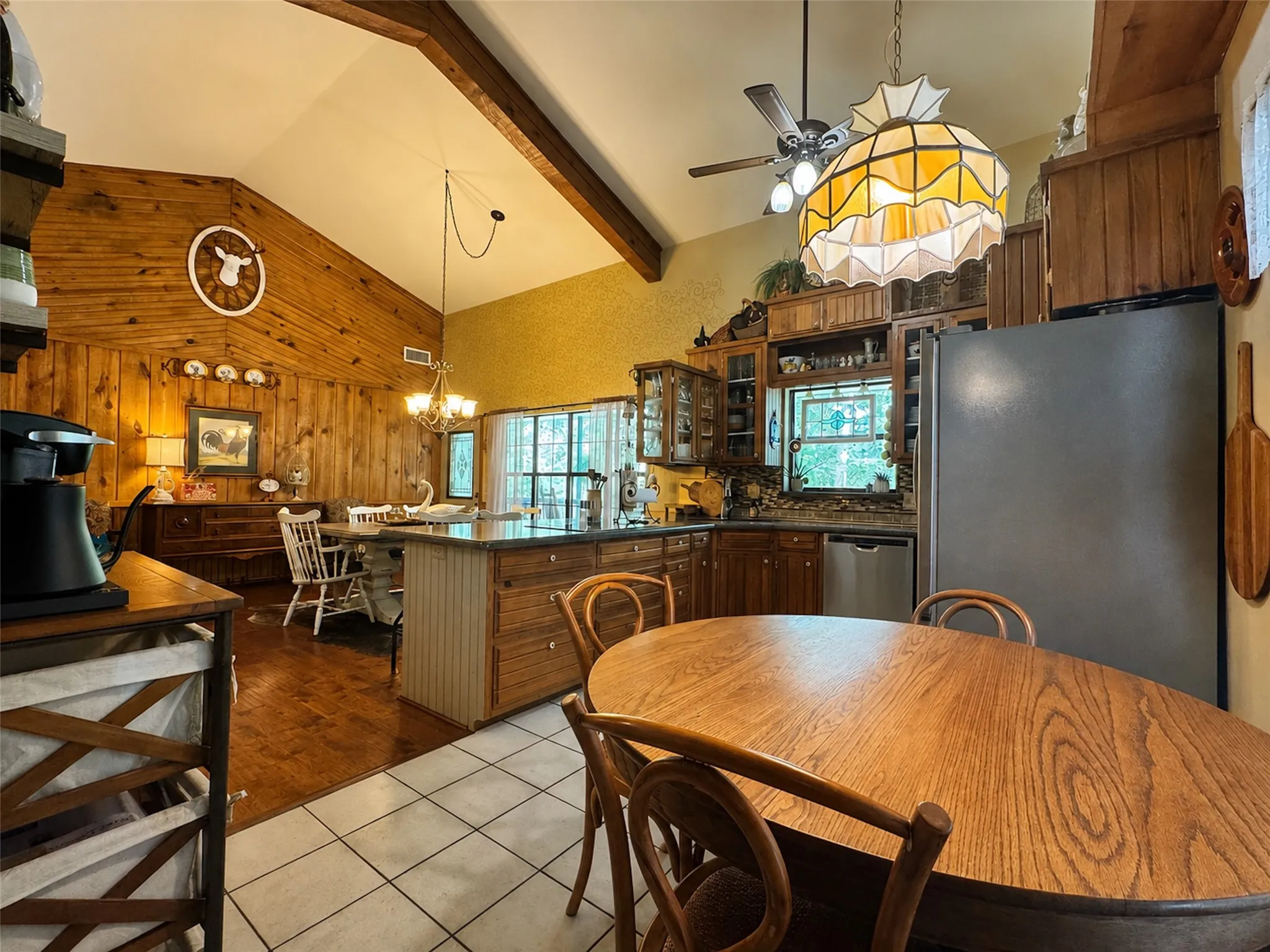 Vaulted ceiling with exposed beams, wood-paneled accent wall, wood-finish flooring, kitchen island with built-in cabinetry, and stainless steel appliances