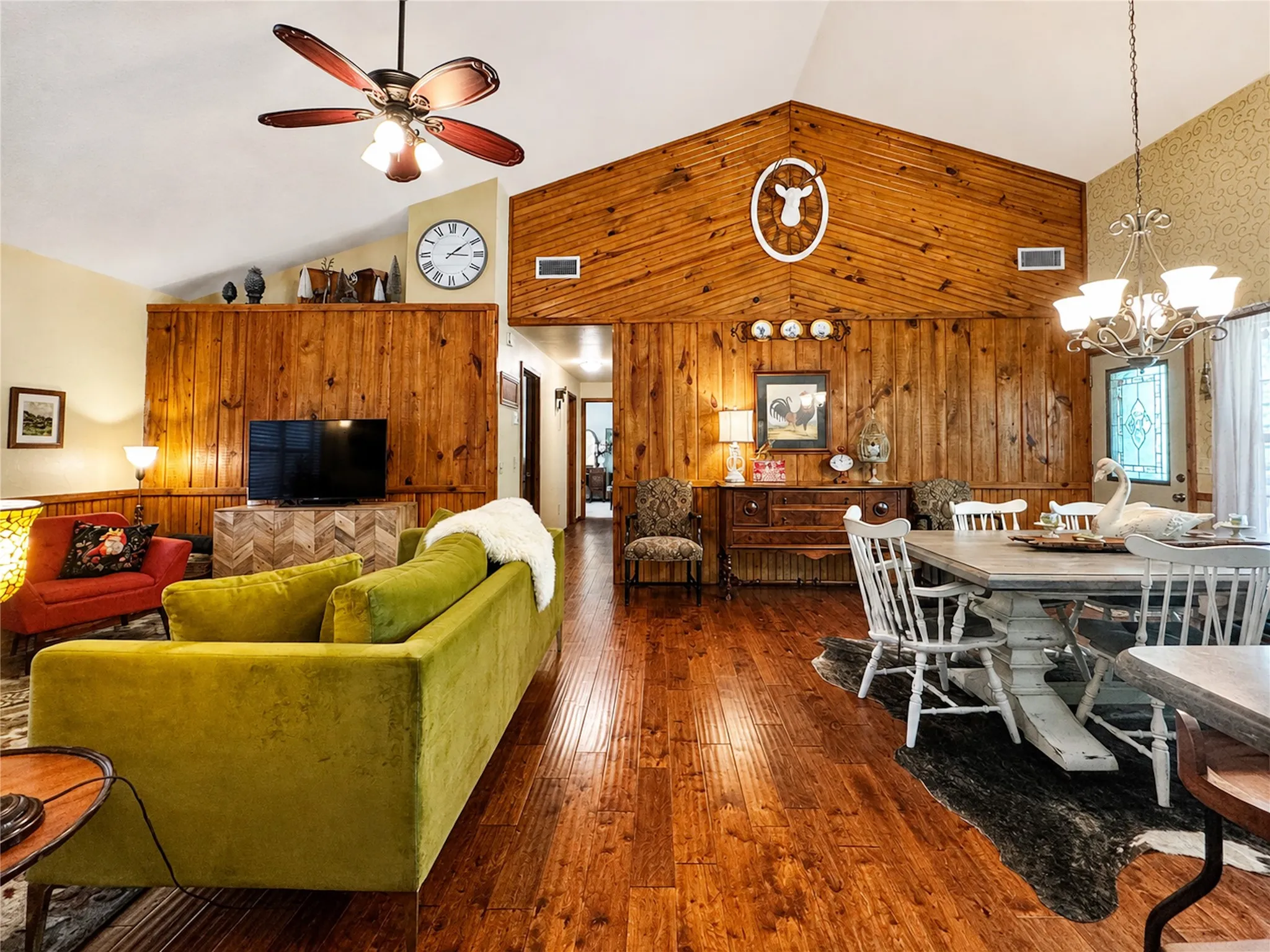 Vaulted ceiling with a ceiling fan, wood-finish flooring, wood panel accent walls, and a chandelier-style light fixture