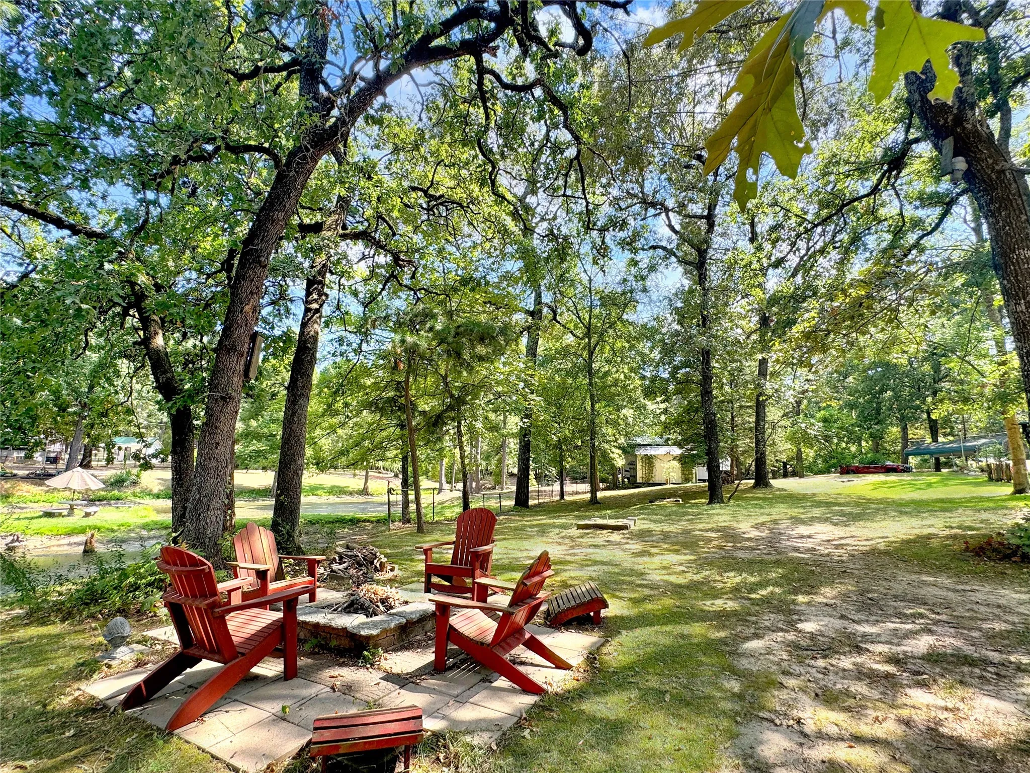 Expansive green space featuring a fire pit with stone surround and mature trees