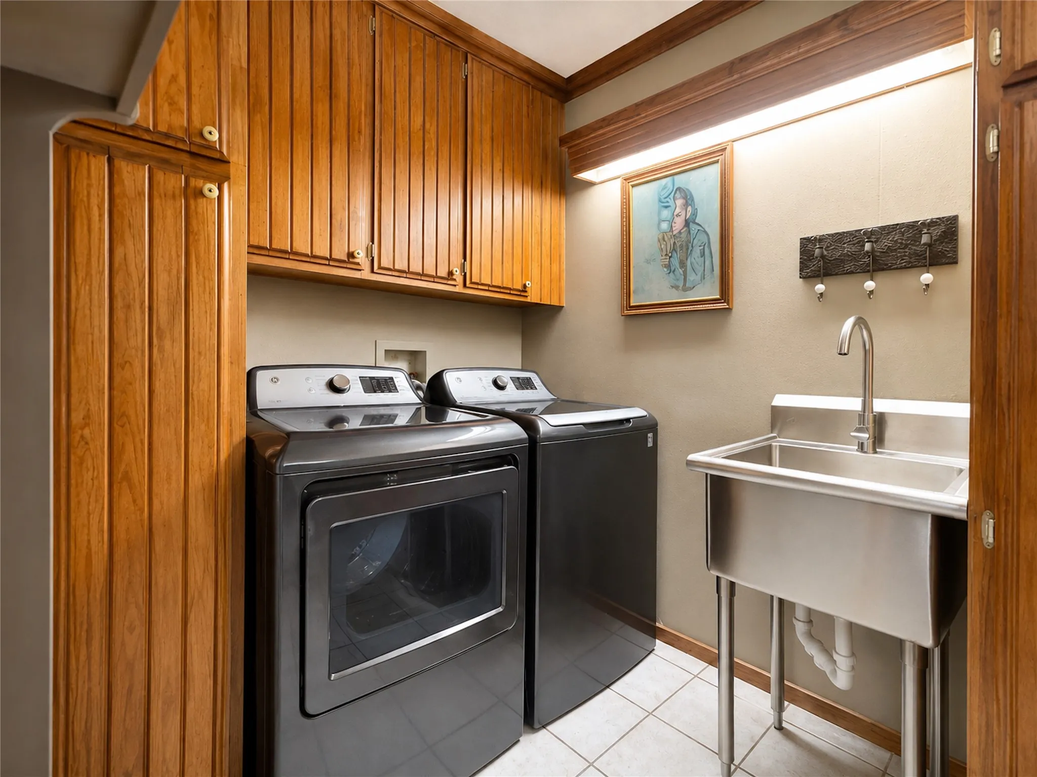 Wood-finish cabinetry, built-in storage, stainless steel utility sink, and tiled flooring