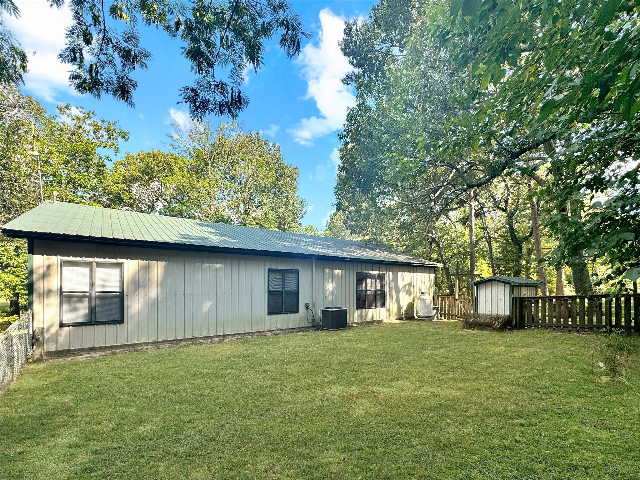 Expansive green lawn with a wood fence, mature trees, and a storage shed